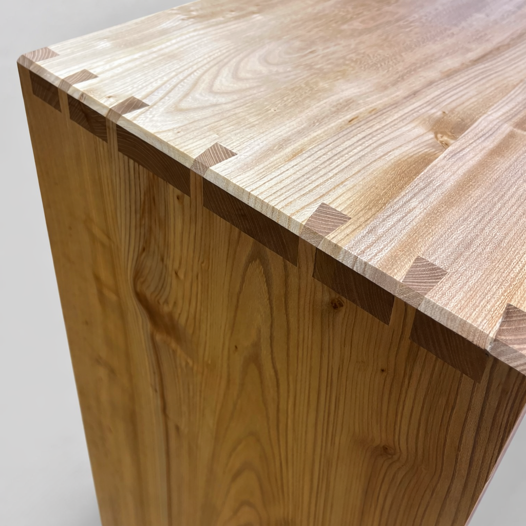 Close-up of a wooden furniture piece with visible dovetail joints on the top corner.
