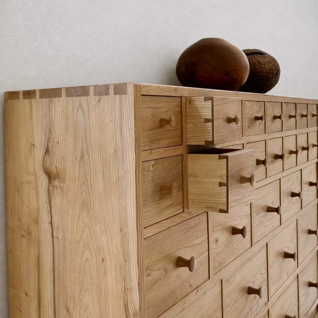 A wooden dresser with multiple small drawers, some open, and three wooden bowls placed on top.
