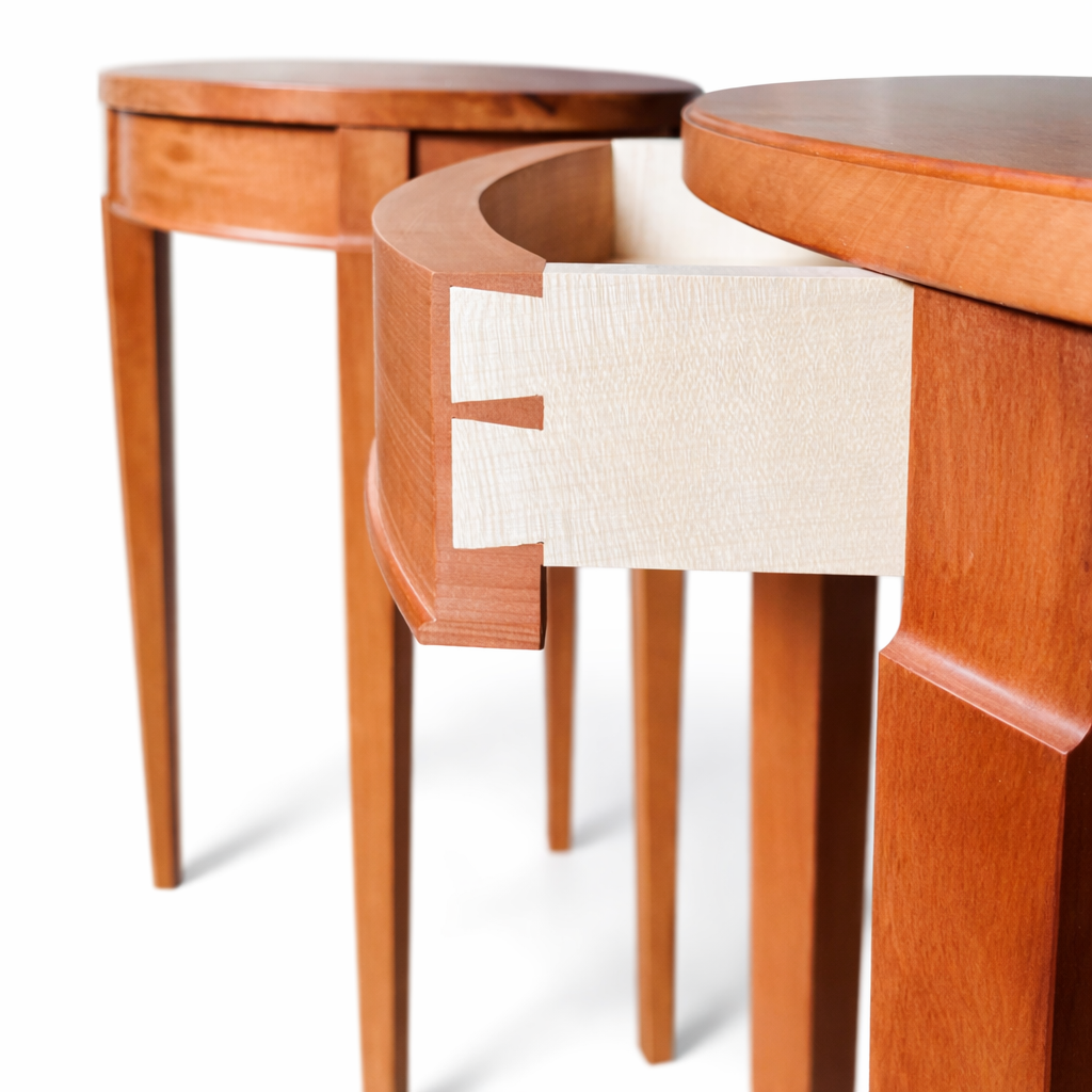 Close-up of two wooden tables with round tops and tapered legs, one smaller and one larger, showing the edge and part of the interior of the smaller table.