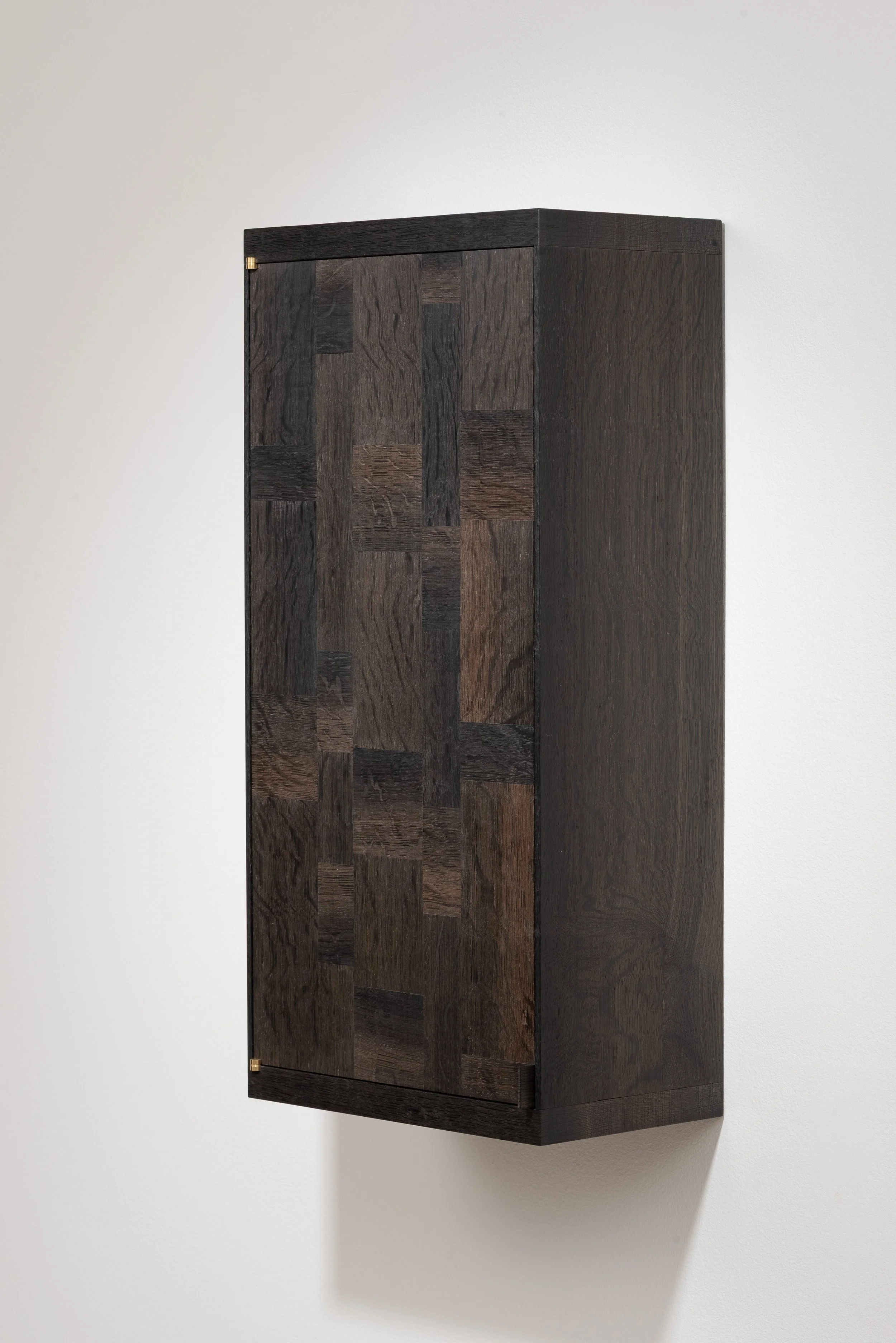 A dark wooden wall-mounted cabinet with a textured pattern on the door, set against a light-colored wall.