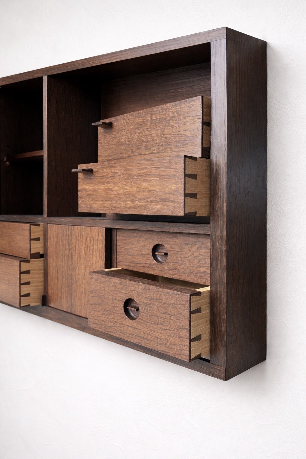 Close-up of a modern wooden cabinet with multiple drawers and compartments, made of dark and light wood, mounted on a white wall.