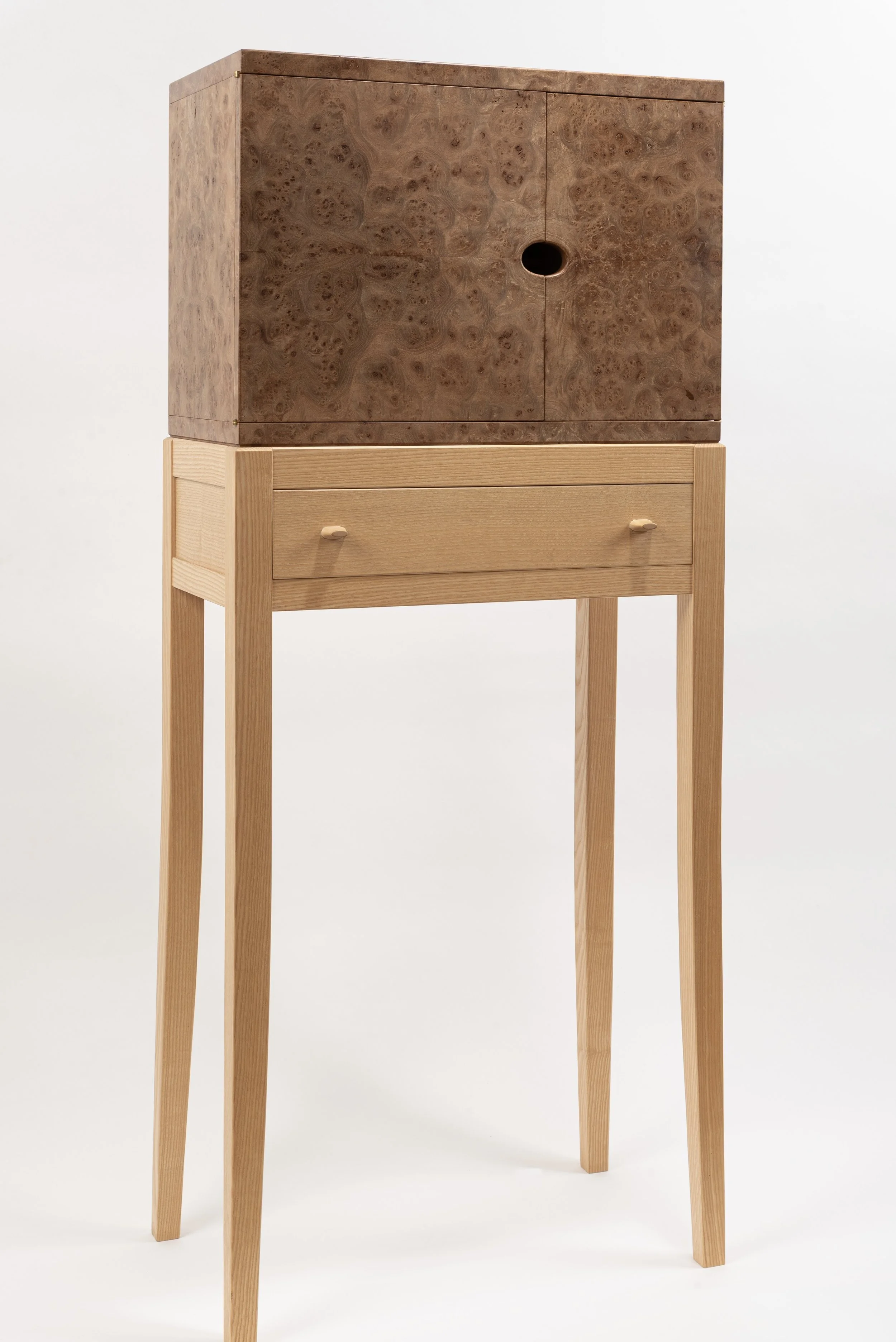 A wooden cabinet with burl wood veneer on top, placed on a light wooden stand with a drawer, against a white background.