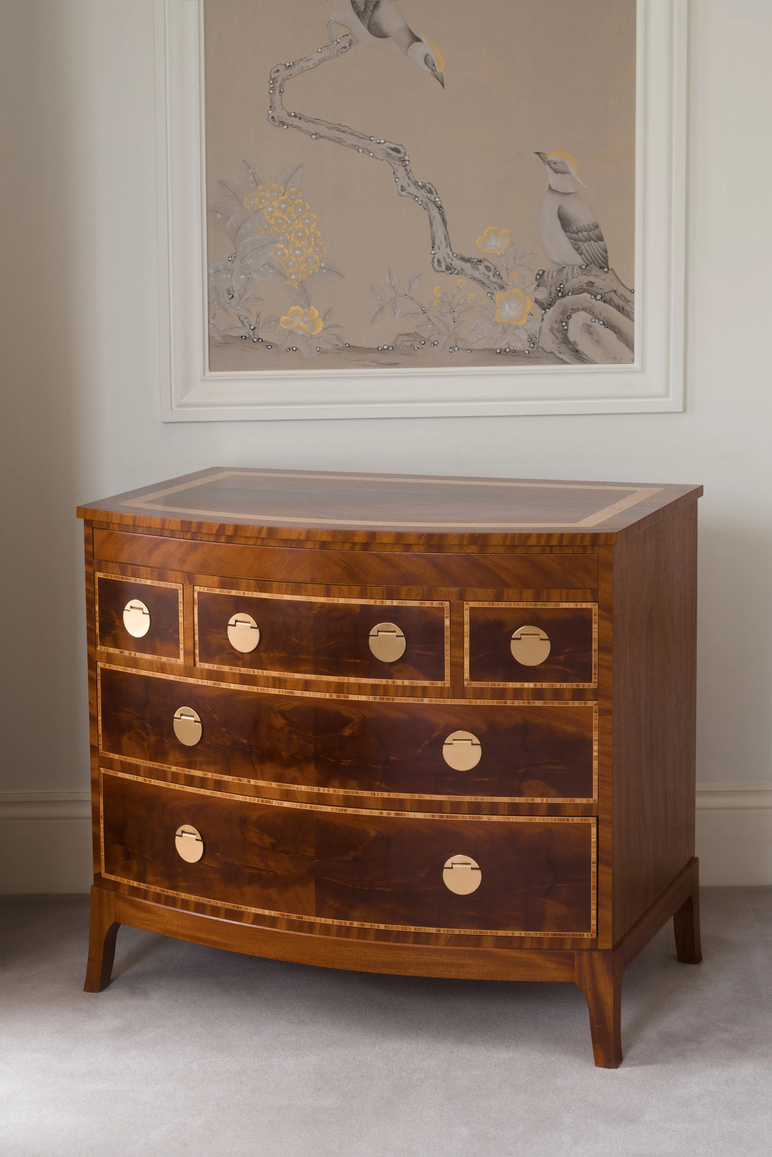 A wooden dresser with six drawers, topped with a smooth, polished surface, standing against a wall underneath framed artwork of birds on branches with flowers.