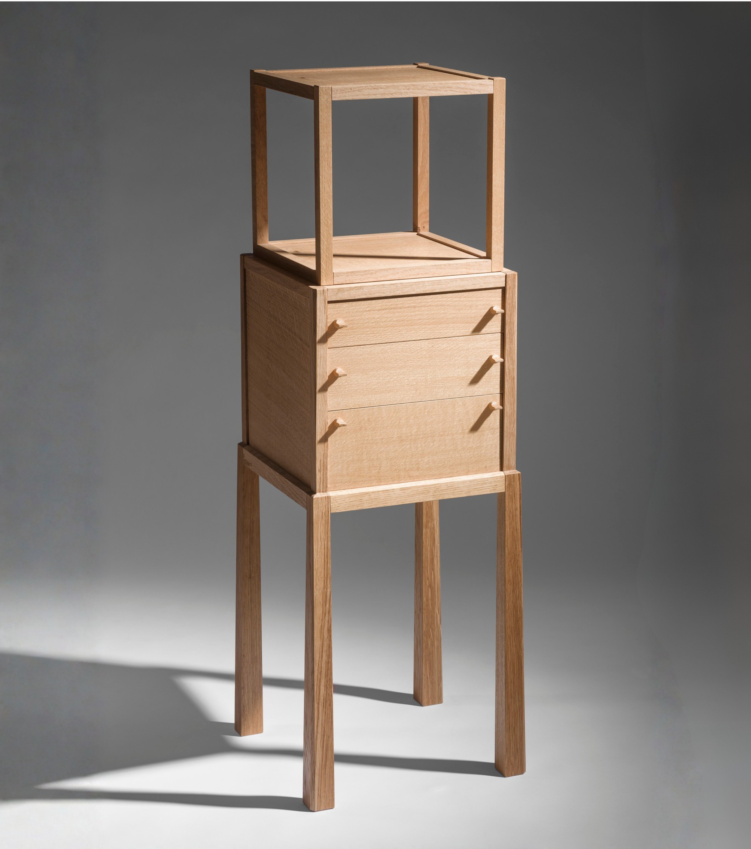 A multi-tier wooden cabinet with four legs, a small drawer unit in the middle, and an open cube frame on top.