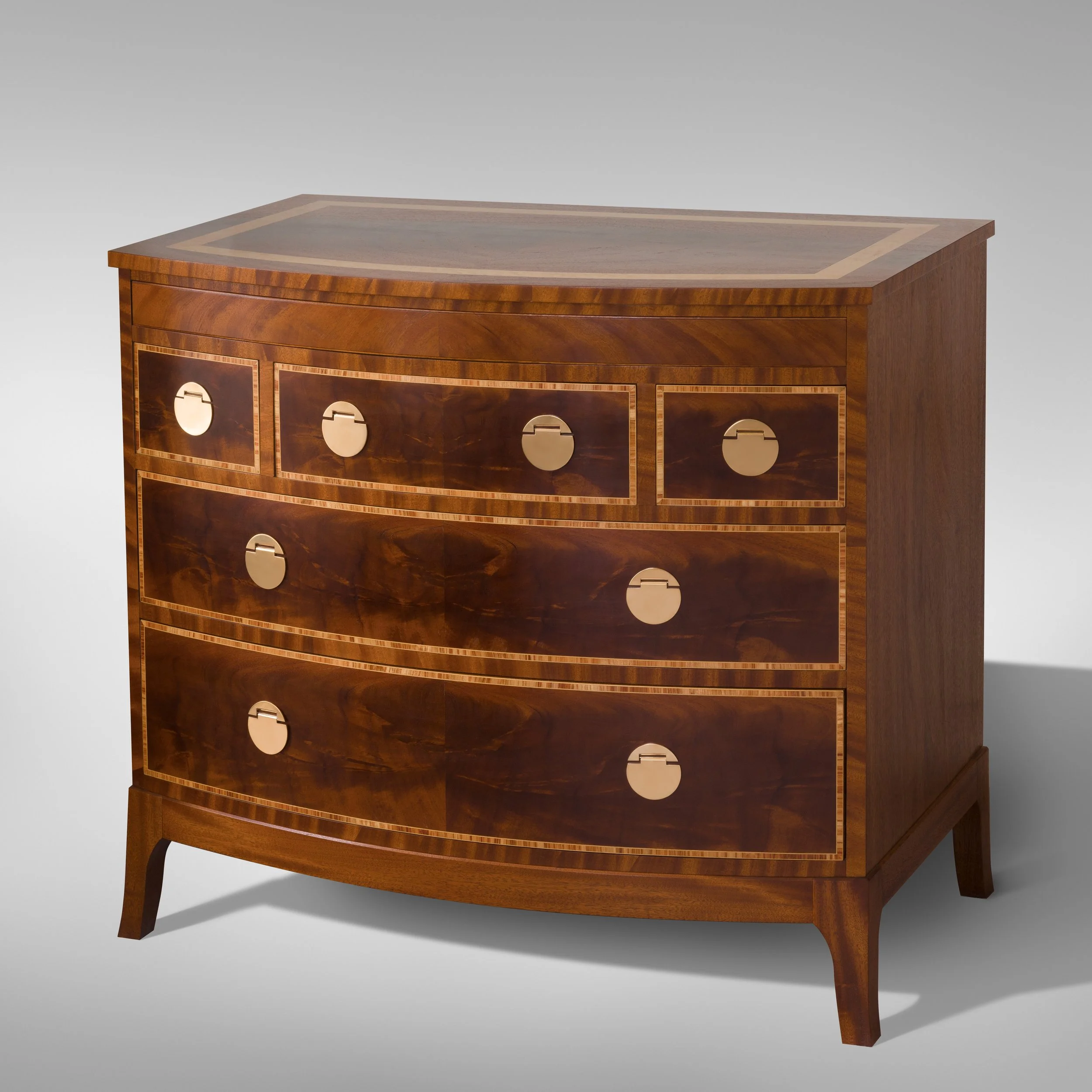 A wooden dresser with a curved front, featuring five drawers with circular metallic handles, set against a plain light gray background.