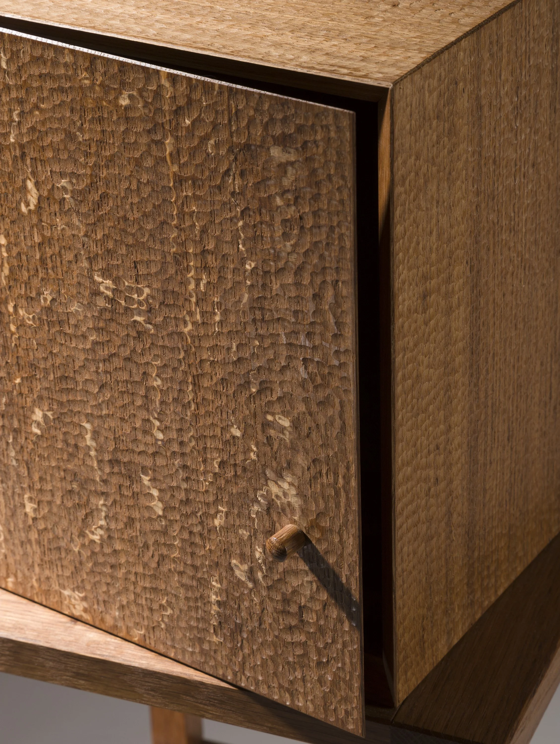 Close-up of a wooden cabinet with a textured, hammered finish on the door and a small wooden knob, partially open.