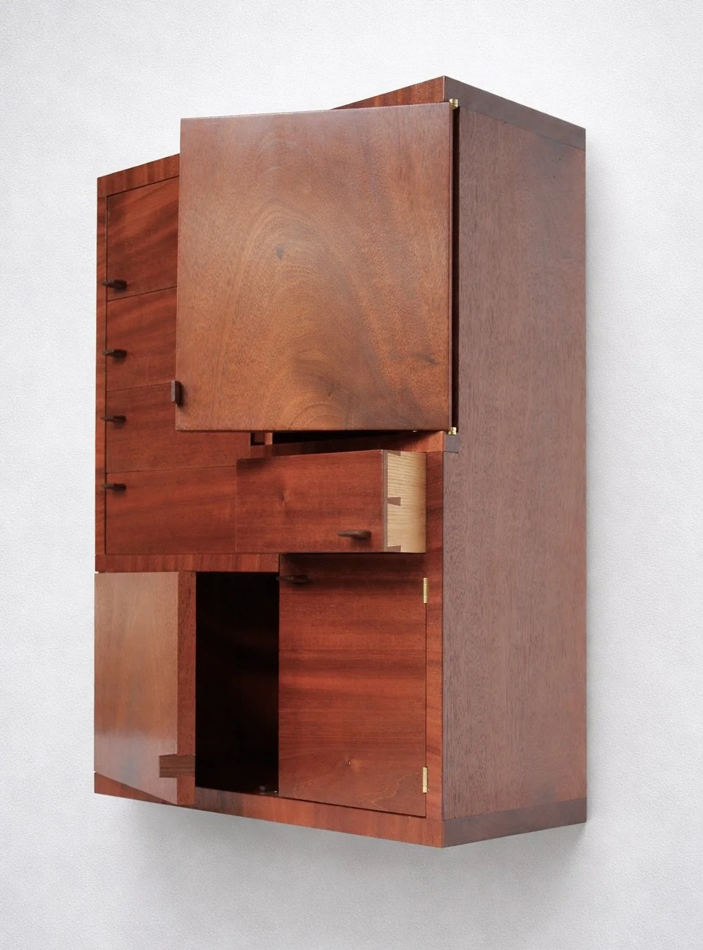A vintage wooden cabinet with multiple compartments and drawers, made of reddish-brown polished wood, mounted on a white wall.