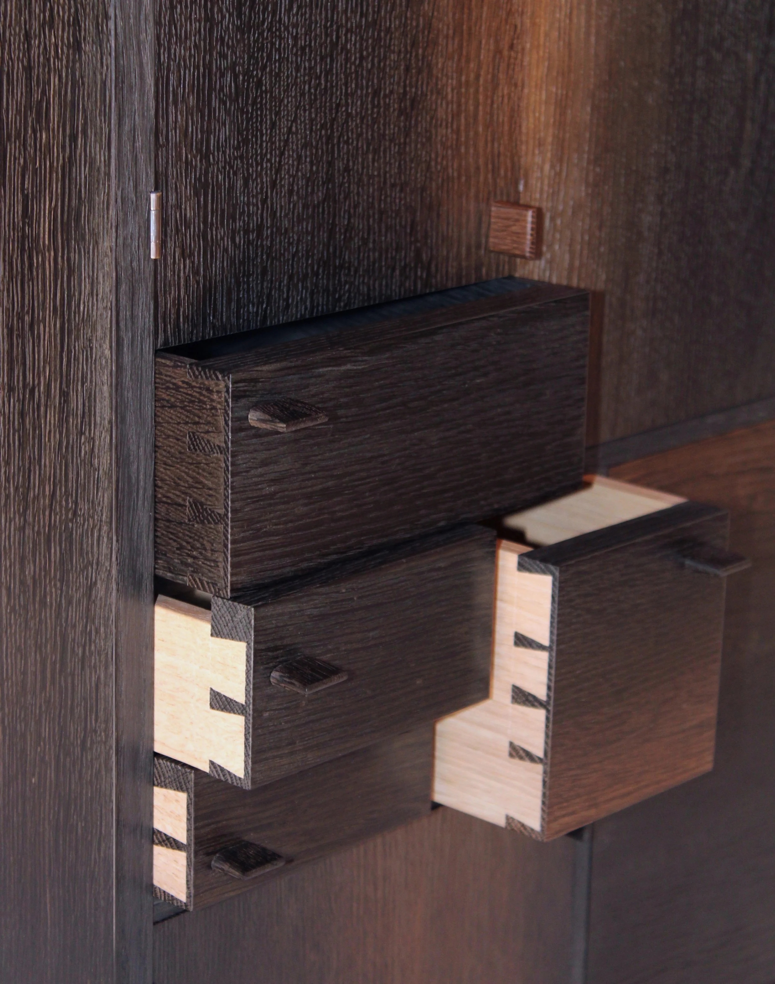 Close-up of a dark wooden cabinet with multiple drawers showing dovetail joints.