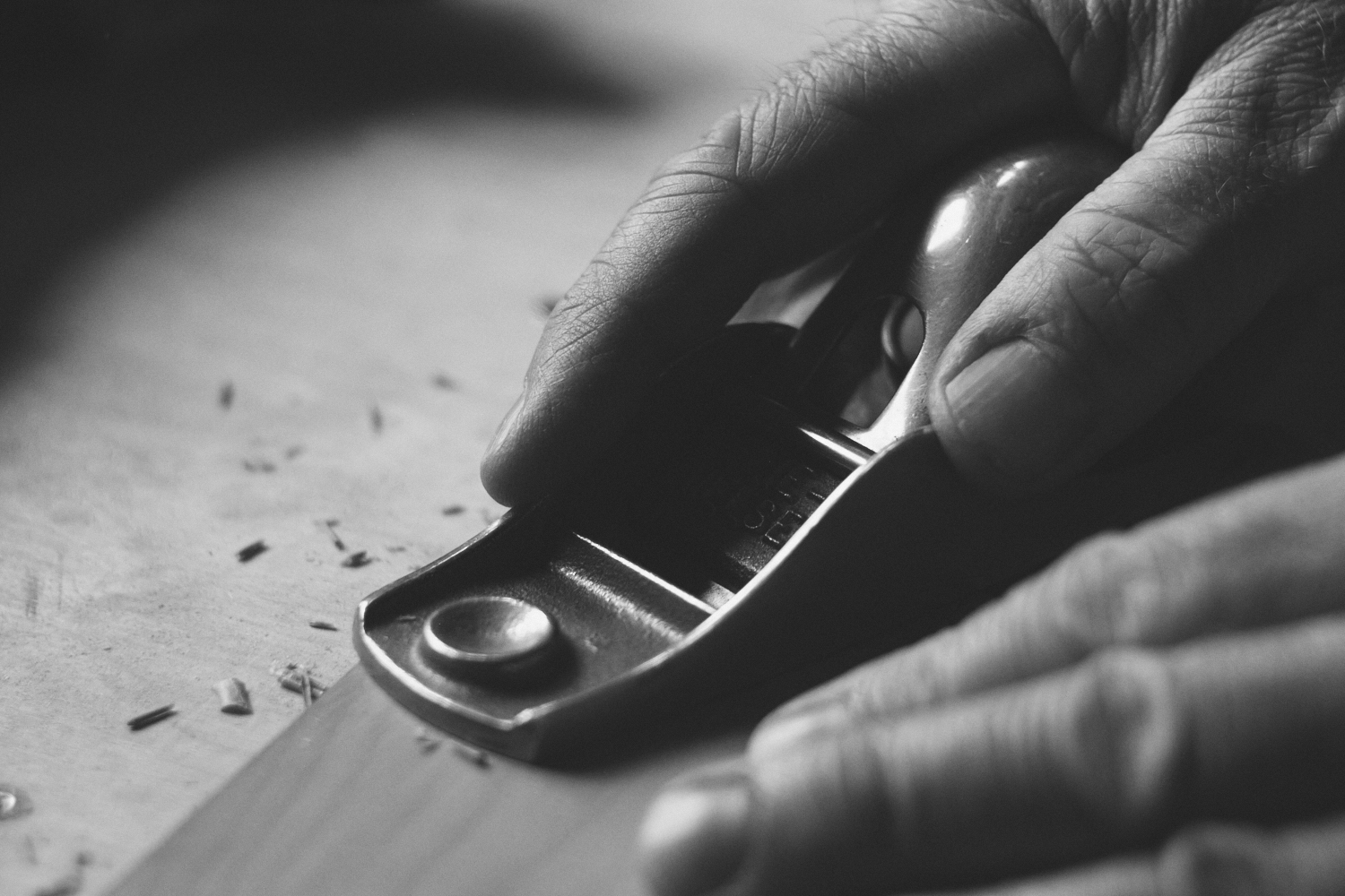 Close-up of a hand using a metal planer on wood in black and white.