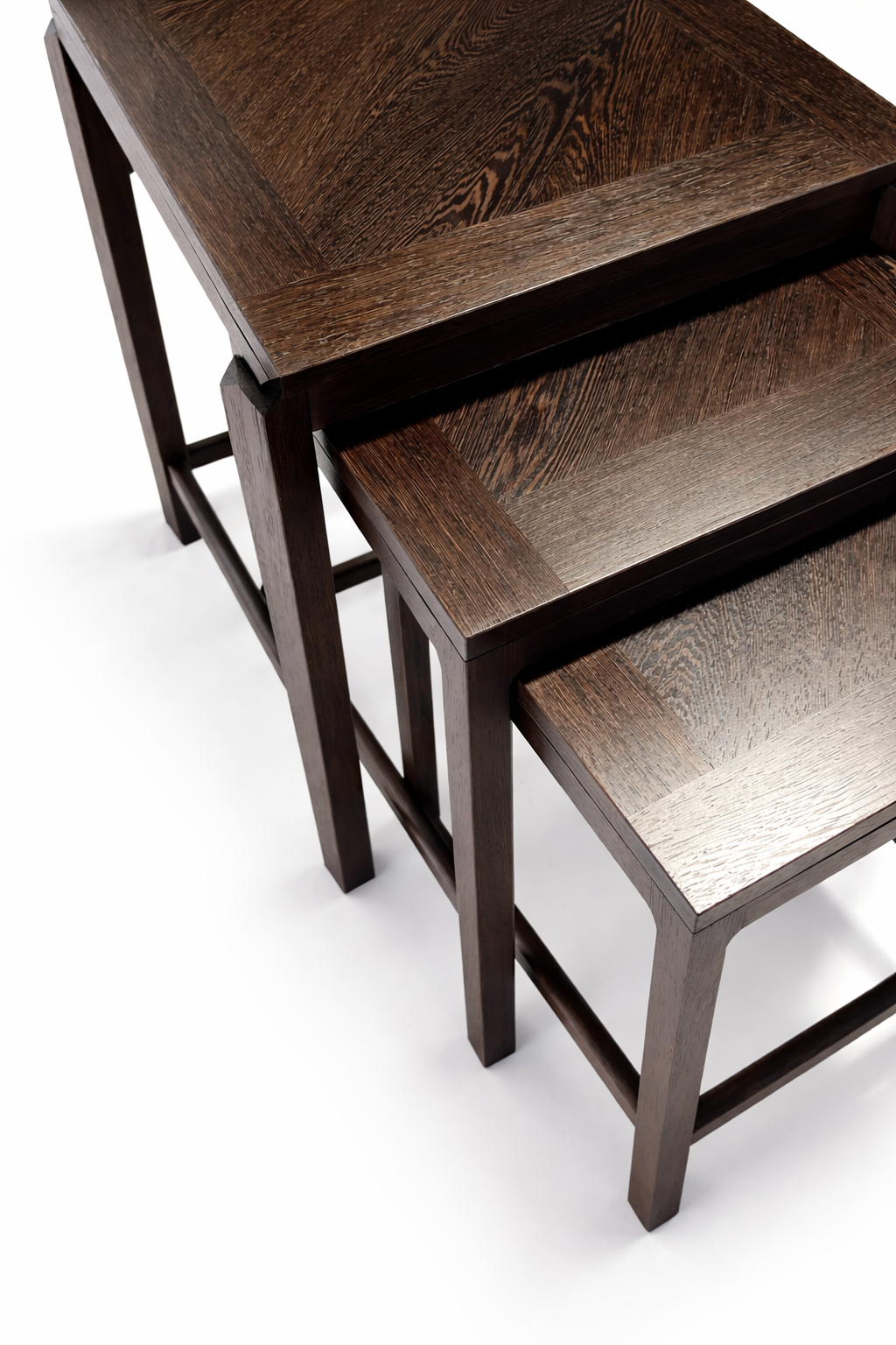 Three dark wood nesting tables with rectangular tabletops and sturdy legs, placed on a white surface.