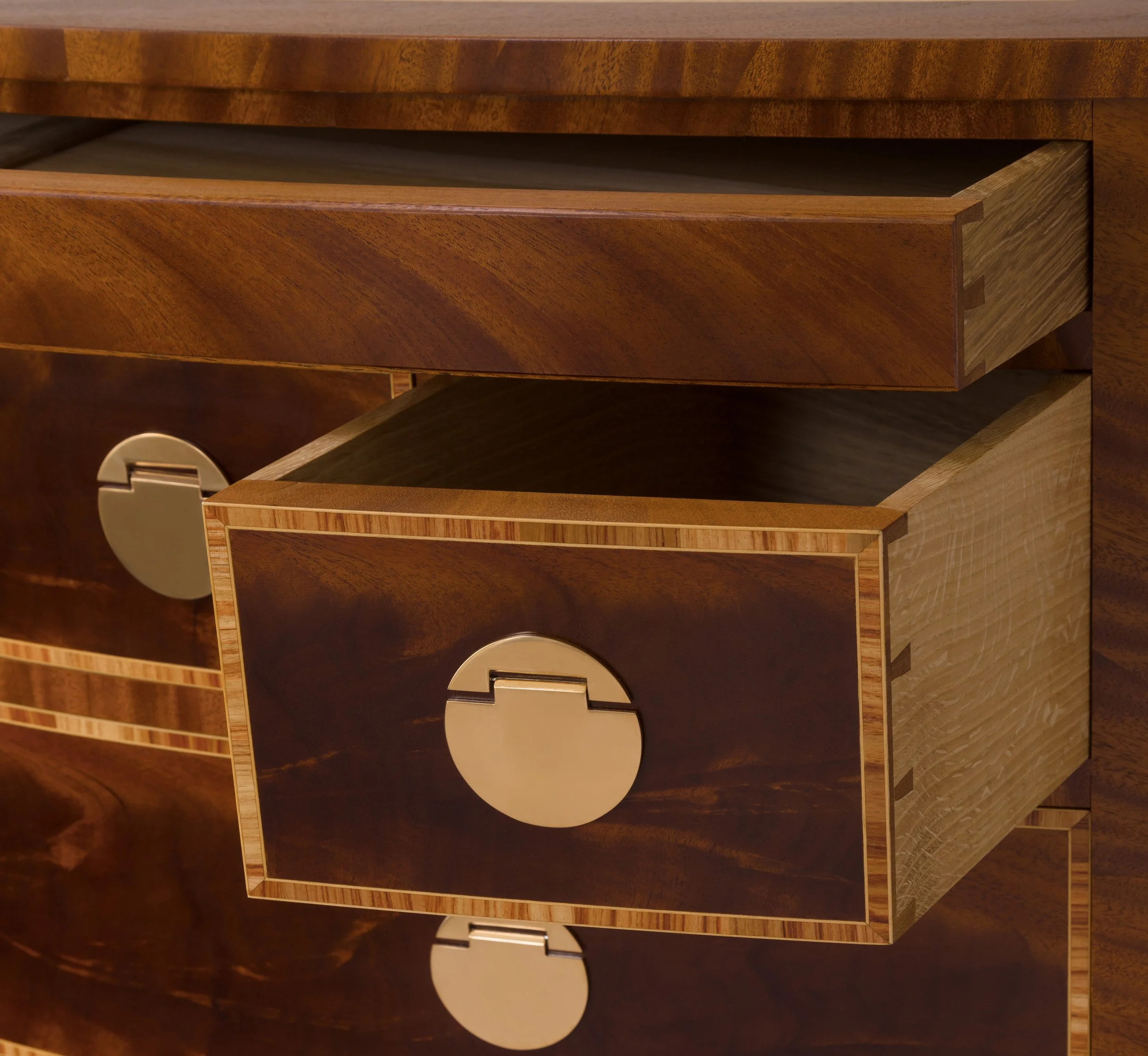 Close-up of a wooden dresser drawer with a metallic round handle, showing intricate wood grain patterns and layered construction.