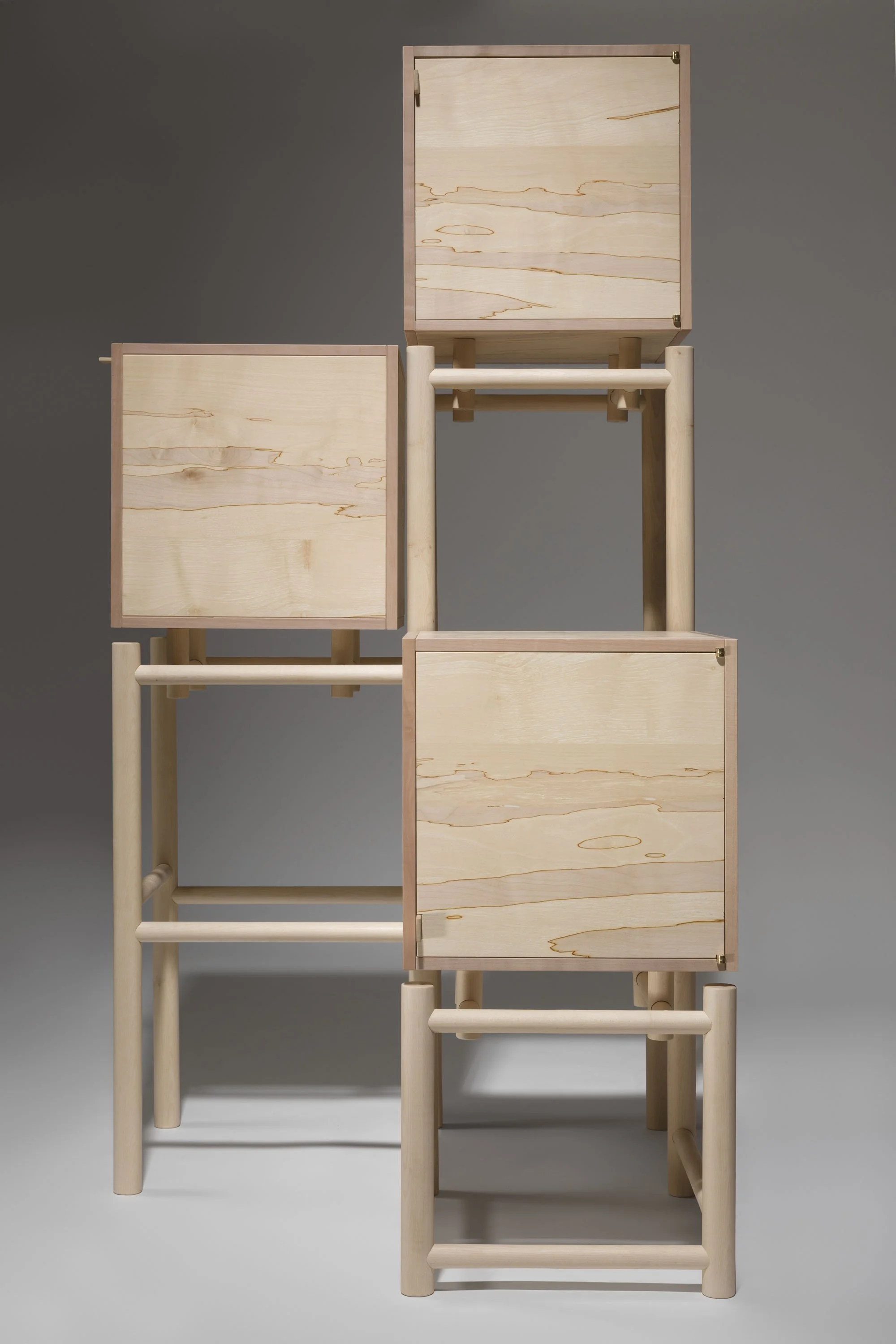 A wooden cabinet with three cubic storage compartments stacked in an asymmetrical configuration, against a plain grey background.