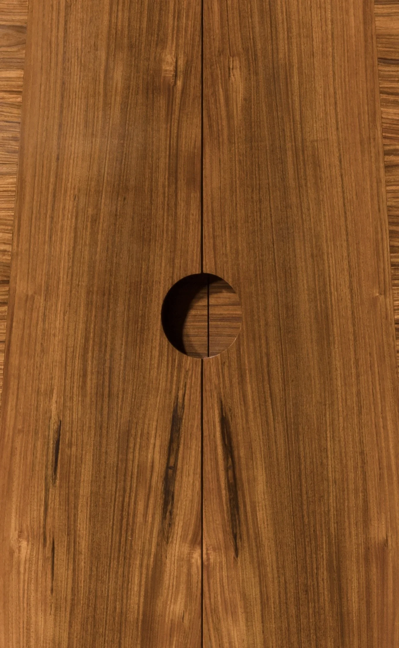 Close-up of a wooden surface with a circular cutout and a central seam.
