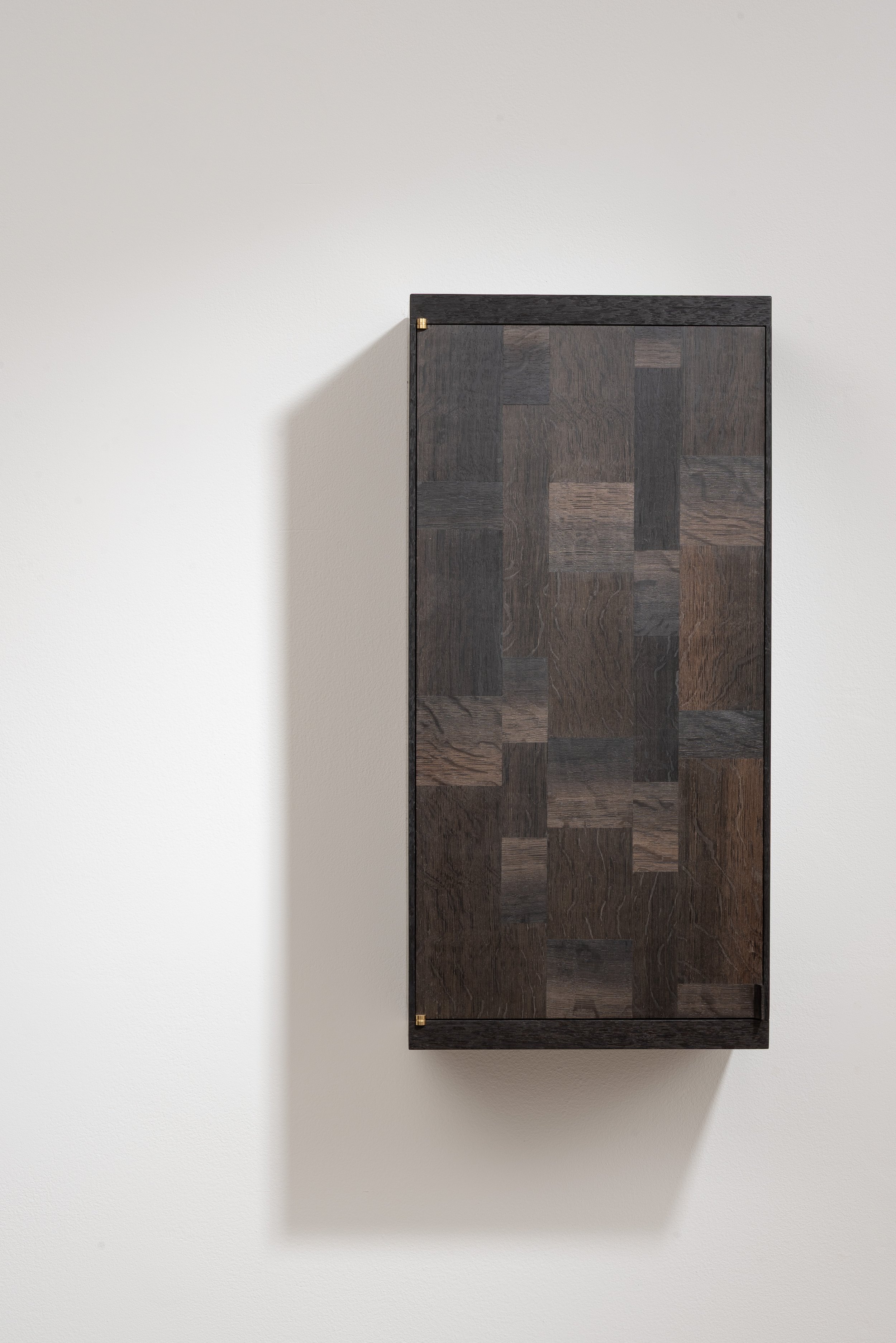 Minimalist dark wooden cabinet mounted on a white wall, casting a shadow to the left.