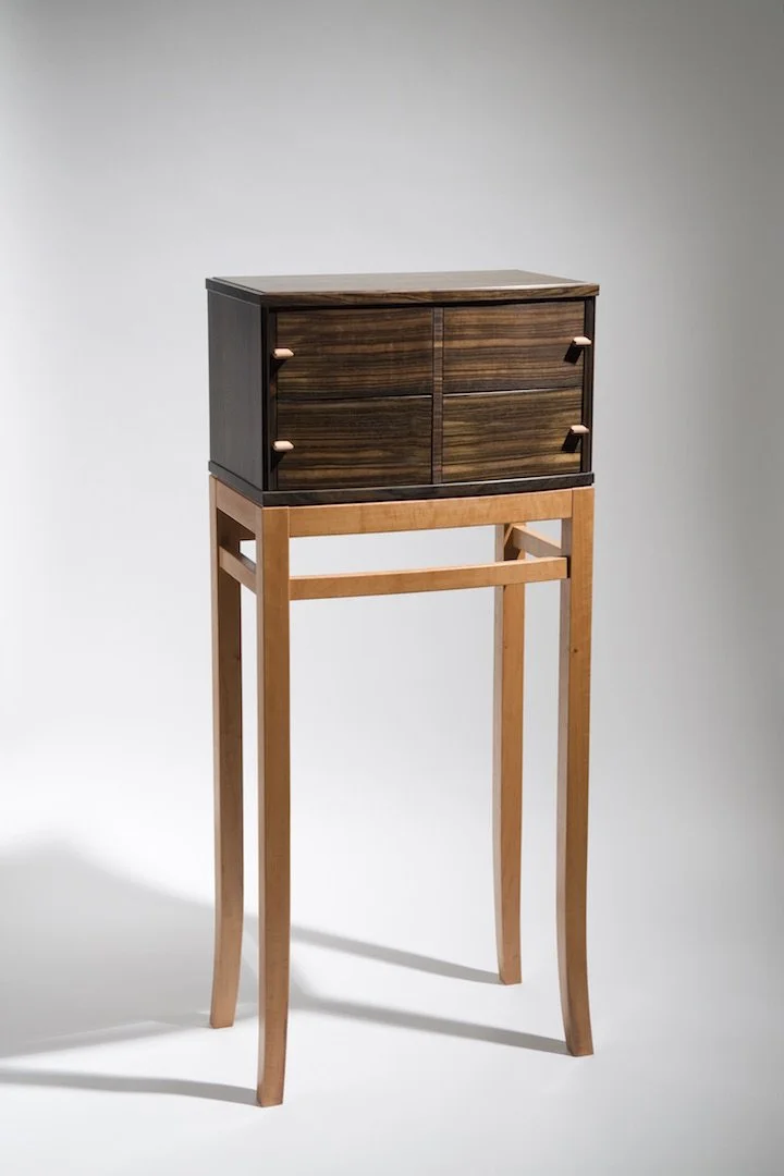 A wooden cabinet with four drawers on a tall, light-colored wooden stand.