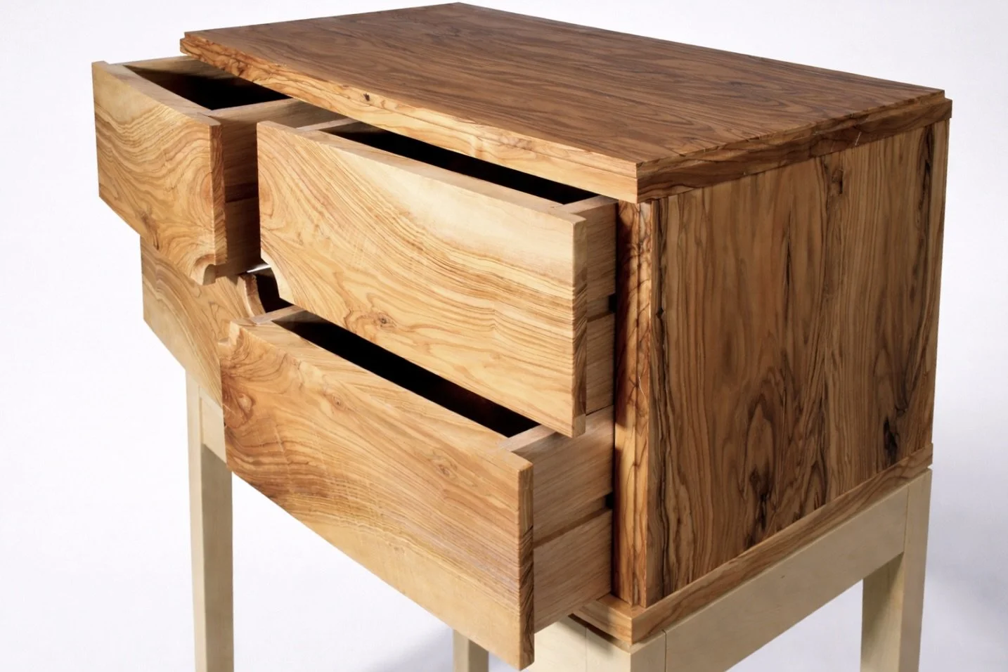 A wooden dresser with three open drawers, made of light-colored, natural wood with a prominent grain pattern, placed on a stand.