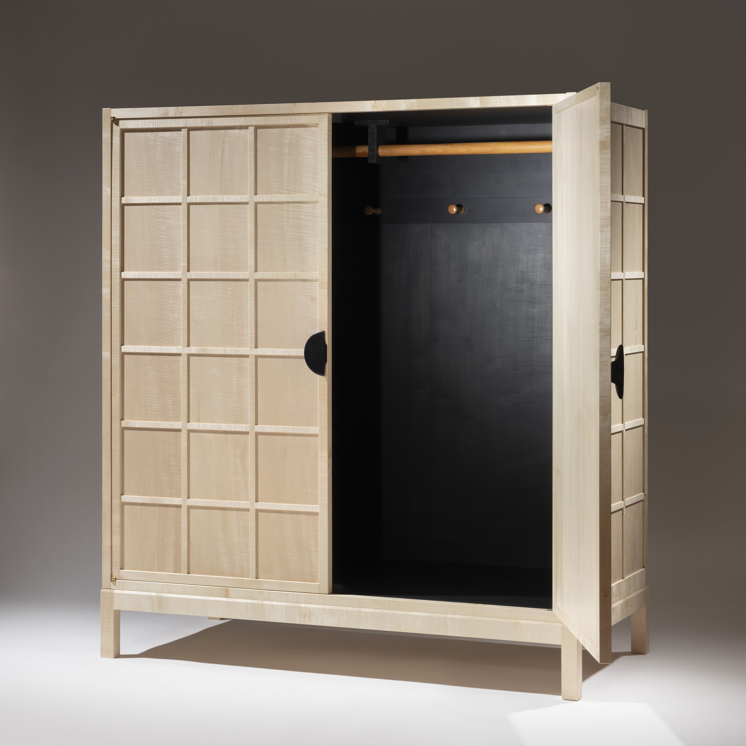 Light-colored wooden wardrobe with two doors, one door open revealing a black interior with a hanging rod and hooks.