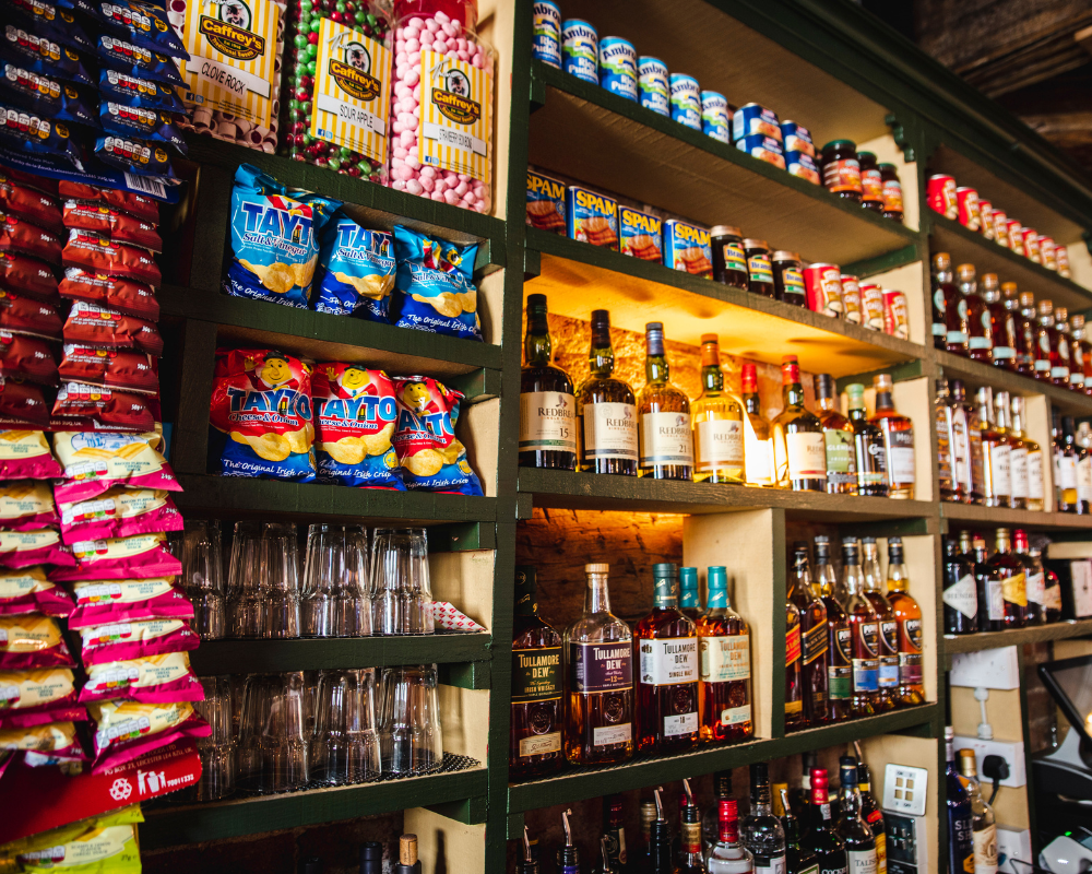 Shelves stocked with snack foods, alcoholic beverages, and condiments in a store.