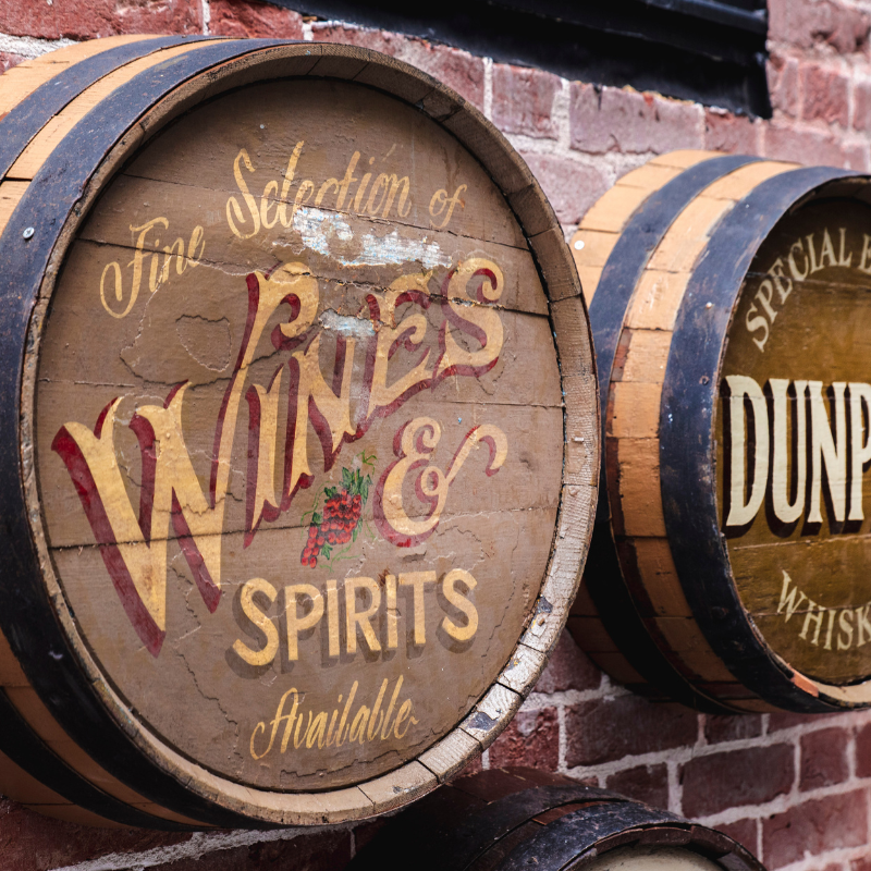 Vintage wooden barrel sign advertising wines and spirits, mounted on a brick wall.