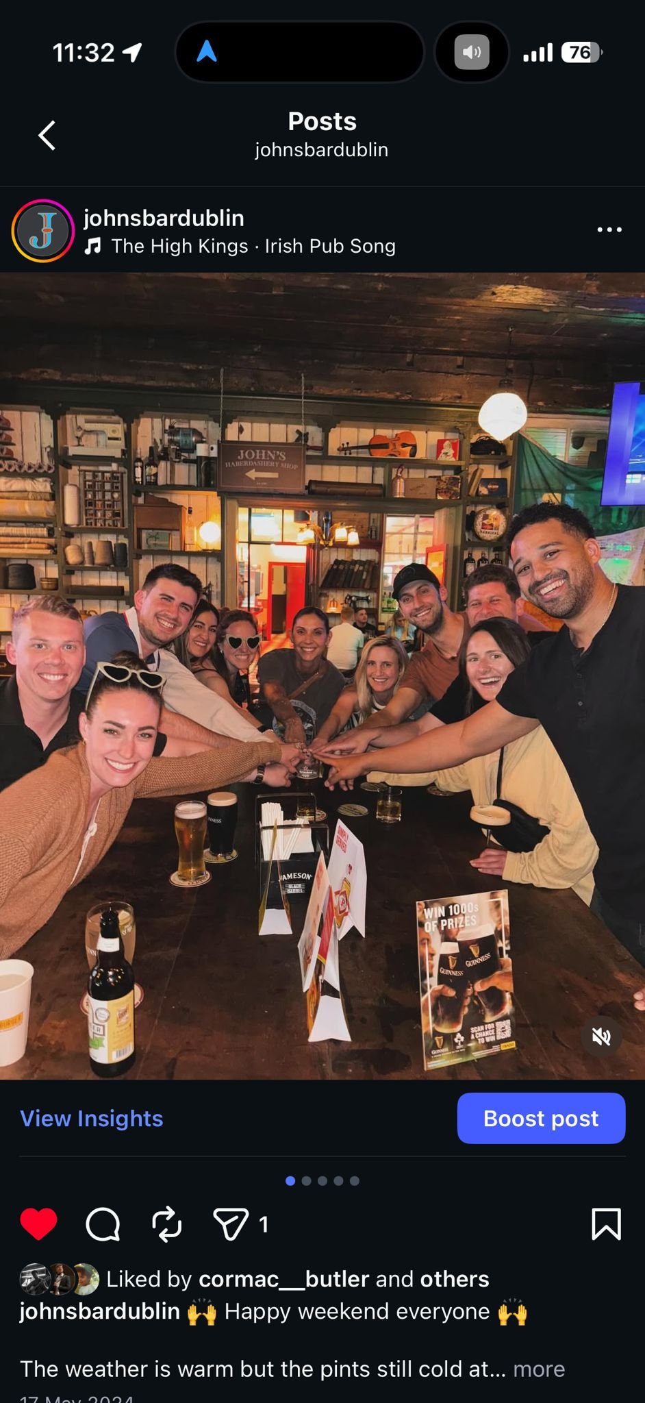 A group of people sitting around a table at a bar, reaching their hands towards the center in a celebratory manner, with drinks on the table and a pub-like interior in the background.