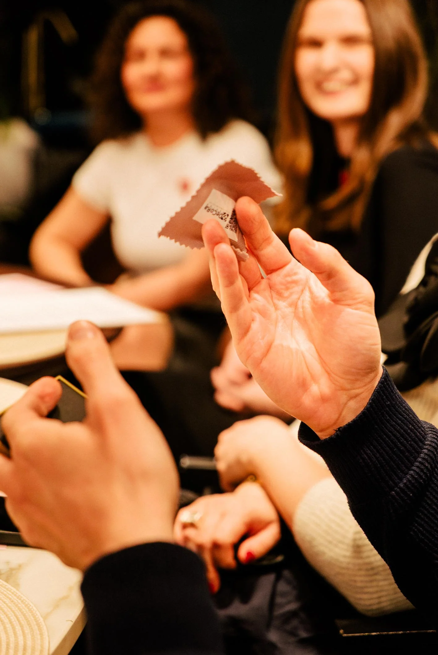A group of people sitting at a table, with some holding and exchanging a small folded piece of paper or card, possibly during a social gathering or meeting.