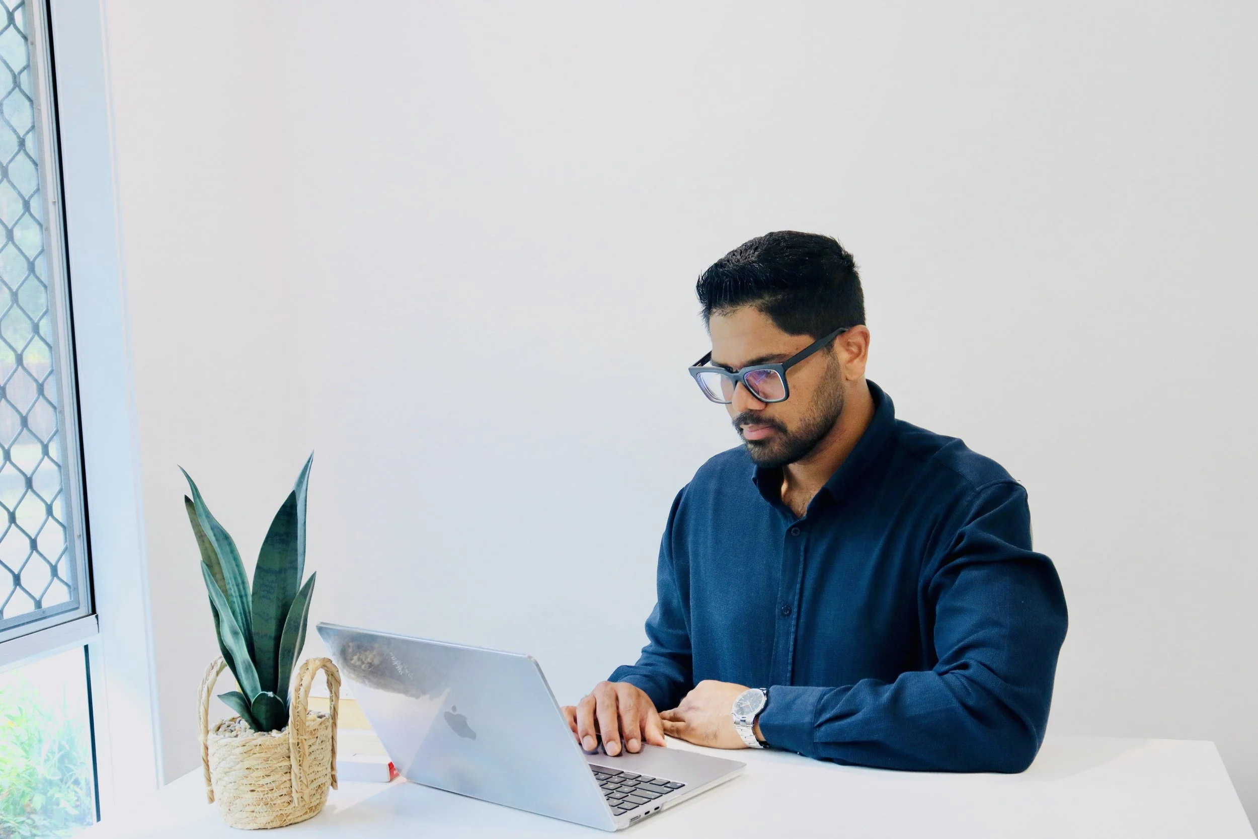 A psychologist working on a laptop in a bright office space with plants, representing telehealth and professional psychological services.