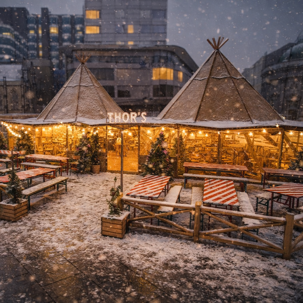 Outdoor snowy scene with a brightly lit Christmas market hut decorated with Christmas trees, benches, and clouds of snow in an urban area.