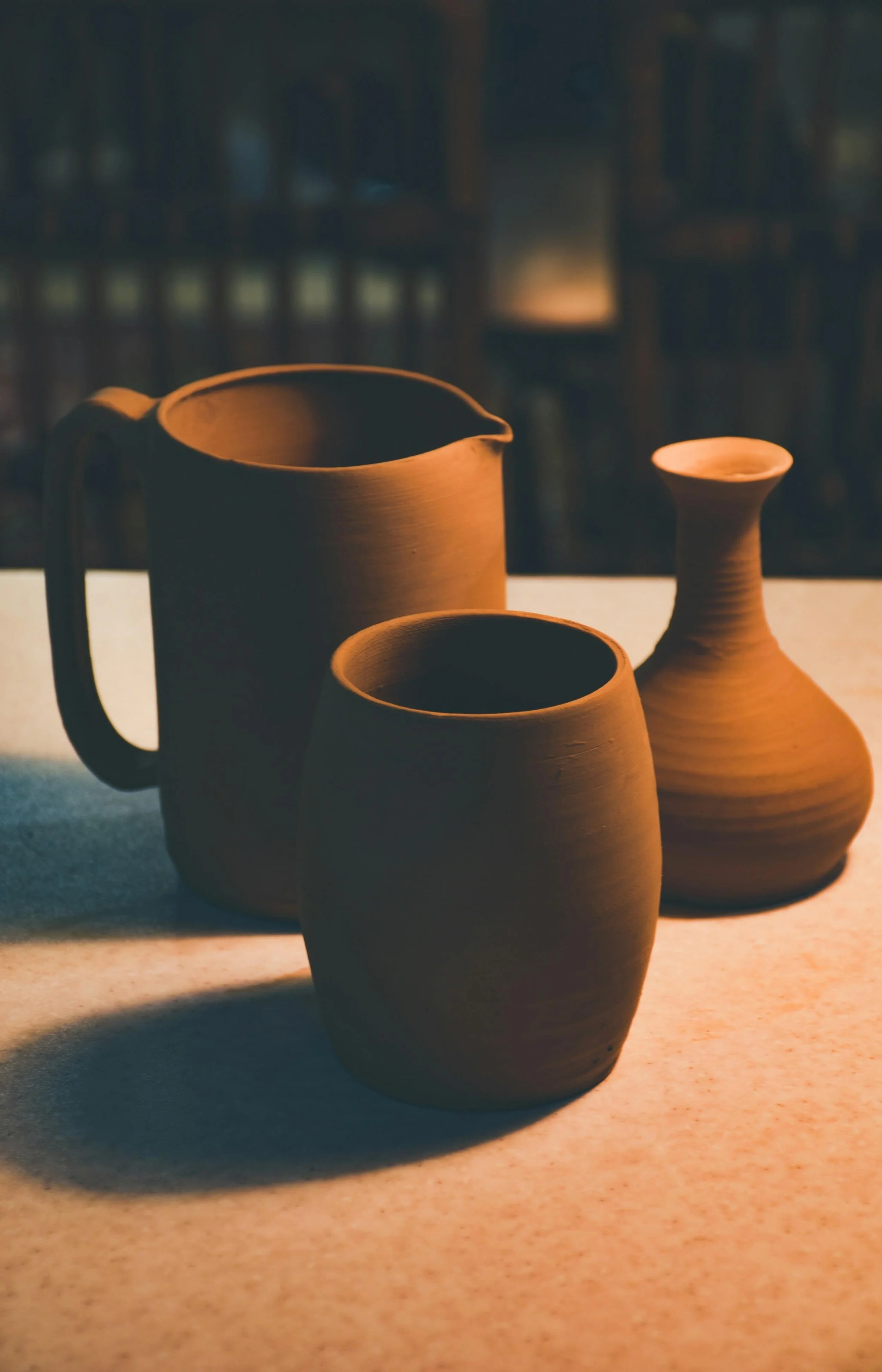 Three clay pottery vessels of different shapes and sizes on a table, with warm lighting creating shadows.