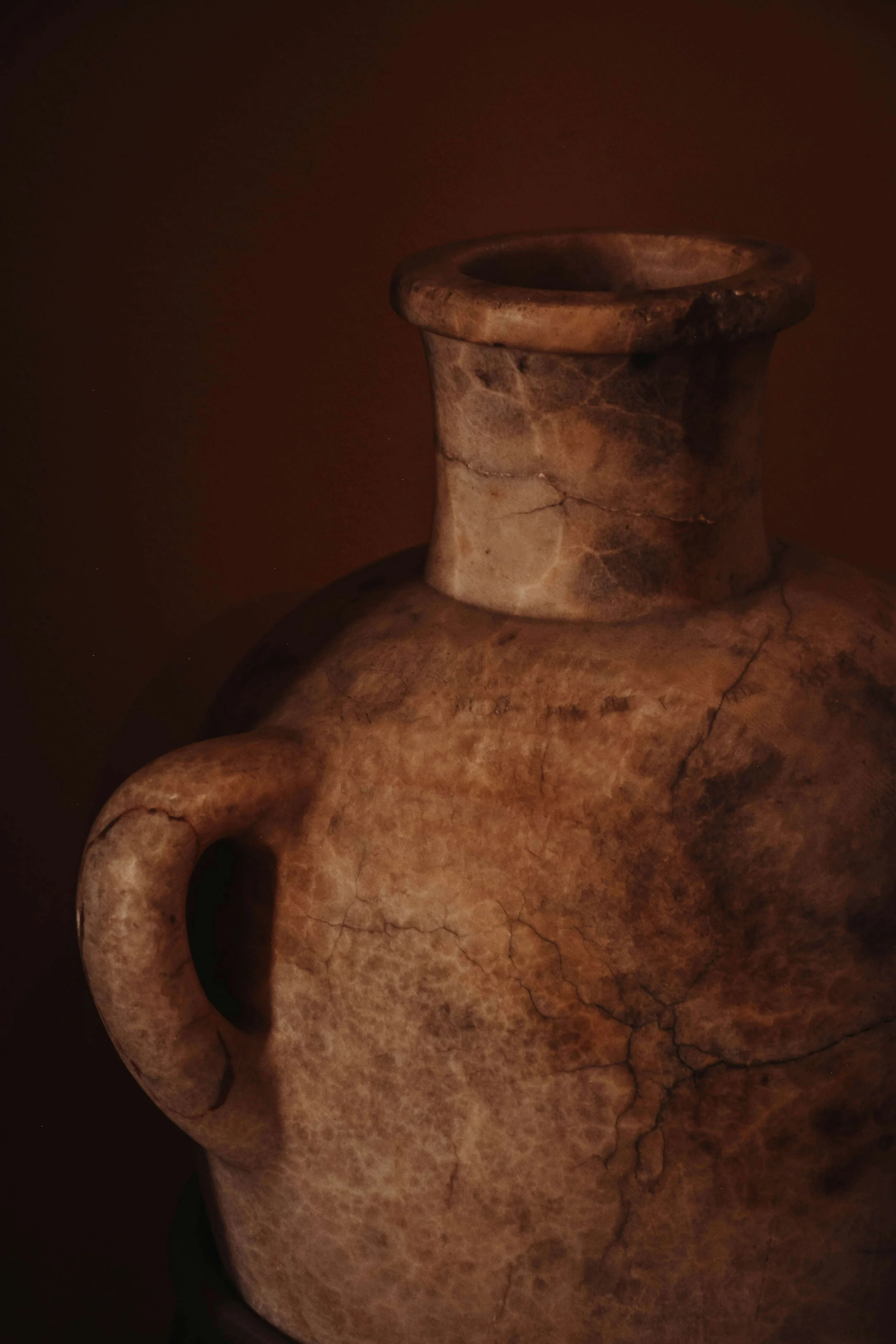 Ancient clay vessel with a handle and wide mouth, exhibiting cracks and a weathered surface.