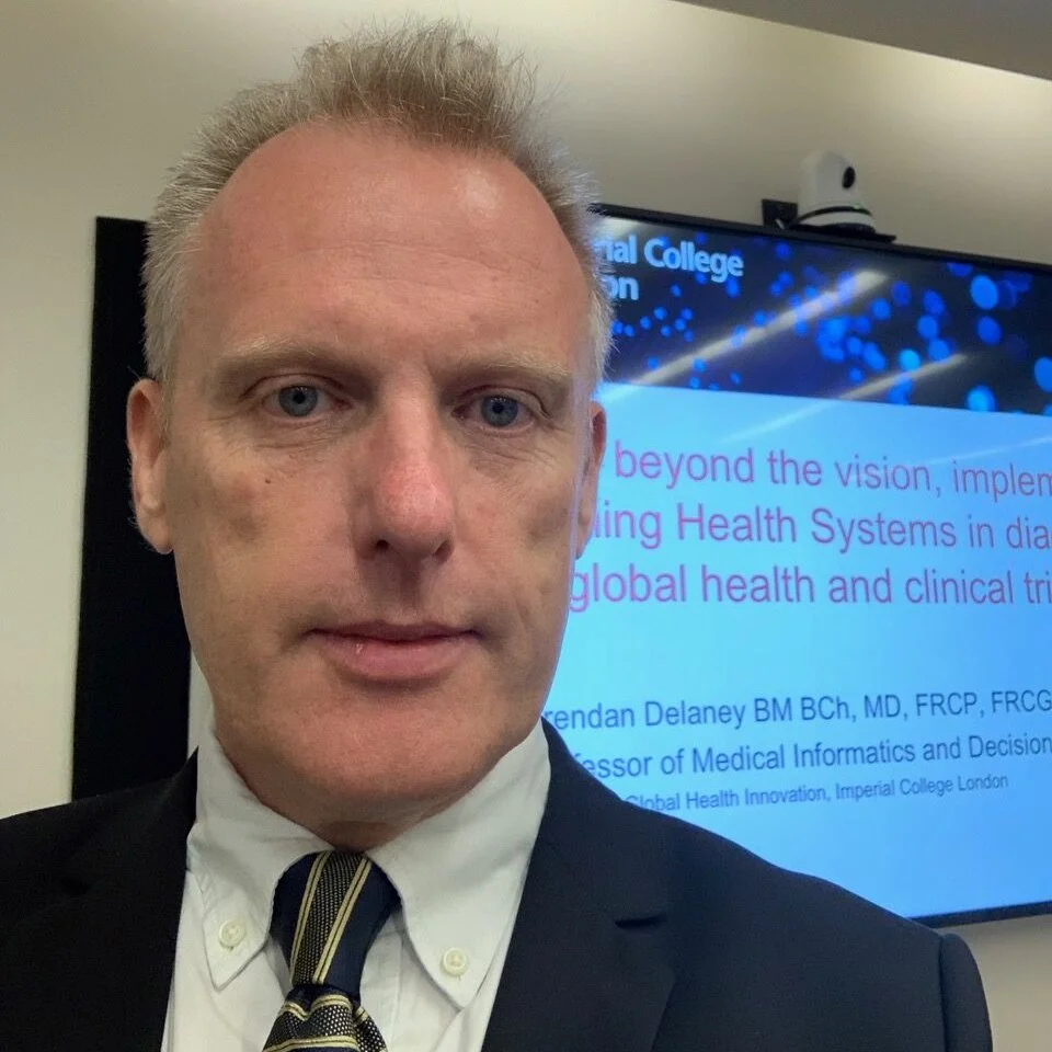 A man in a suit and tie taking a selfie in front of a presentation screen.