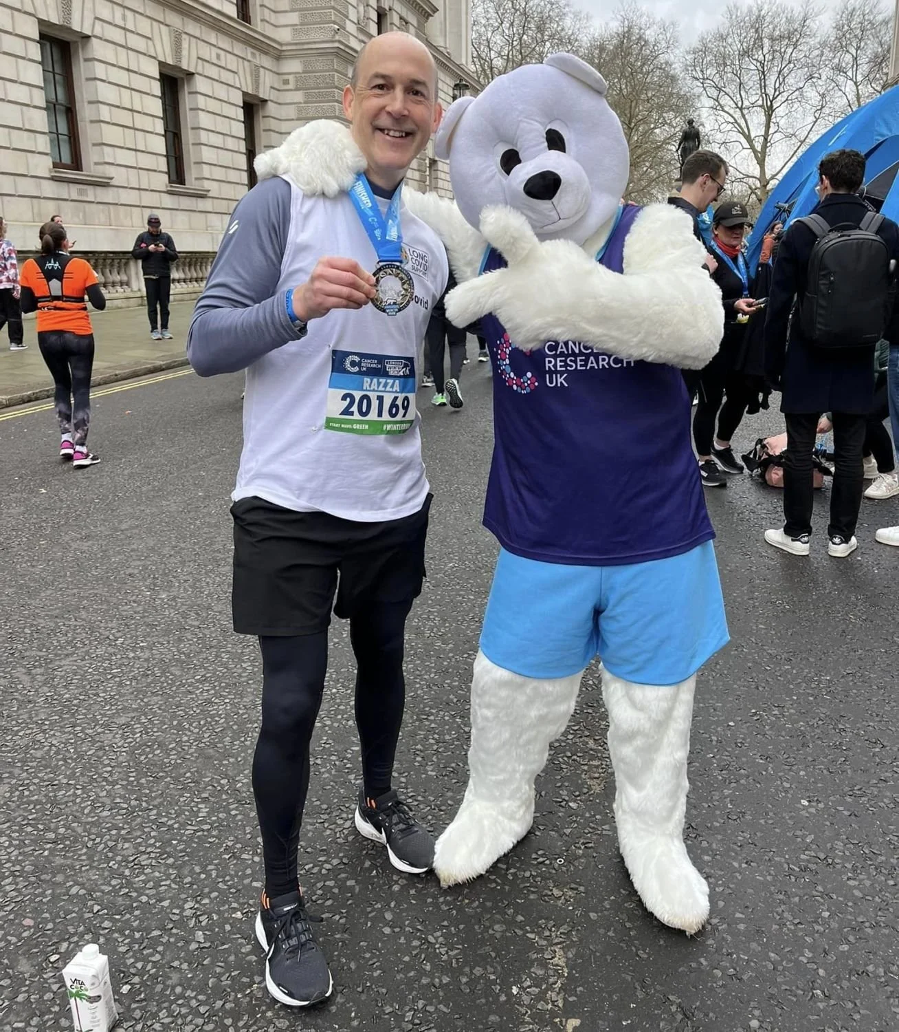 Man in running attire holding a medal, standing next to a person in a polar bear costume at a race event.
