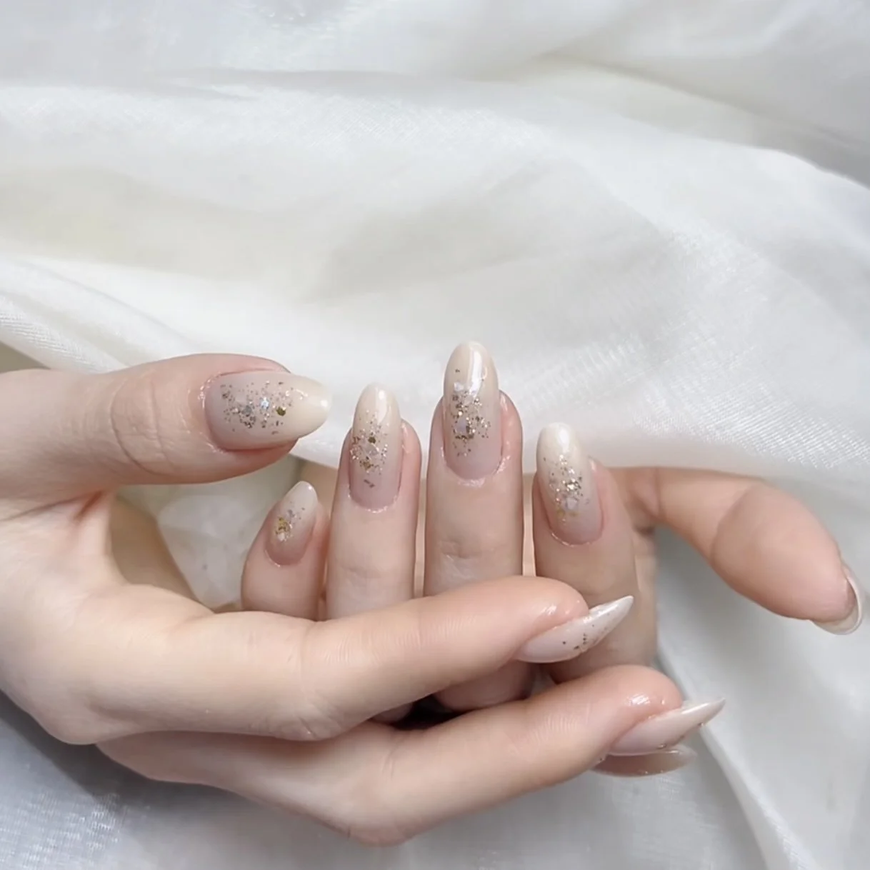 Close-up of a hand with elegant nude nail polish decorated with gold and silver glitter accents.