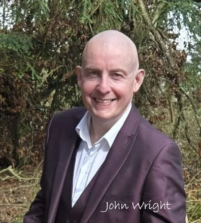 Man in a suit smiling outdoors with trees in the background, with the name John Wright written on the image.