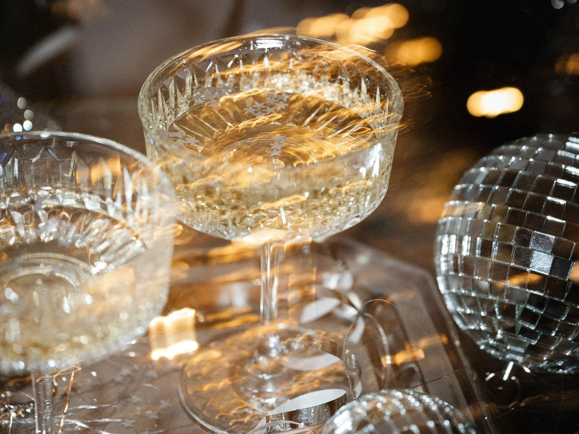 Vasos de vidrio decorativos con estrellas, reflejando luces doradas y plateadas en un ambiente festivo.