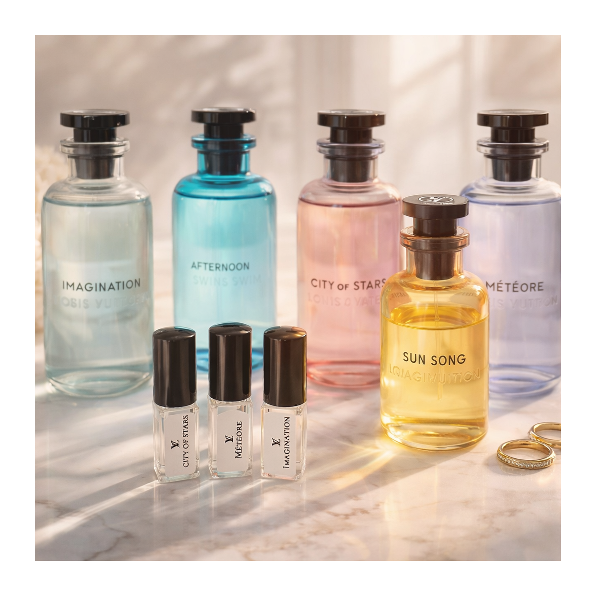 Collection of scented perfume bottles with labels: Imagination, Afternoon, City of Stars, Meteore, and Sun Song, alongside three small perfume sample bottles and a pair of gold rings on a marble surface.