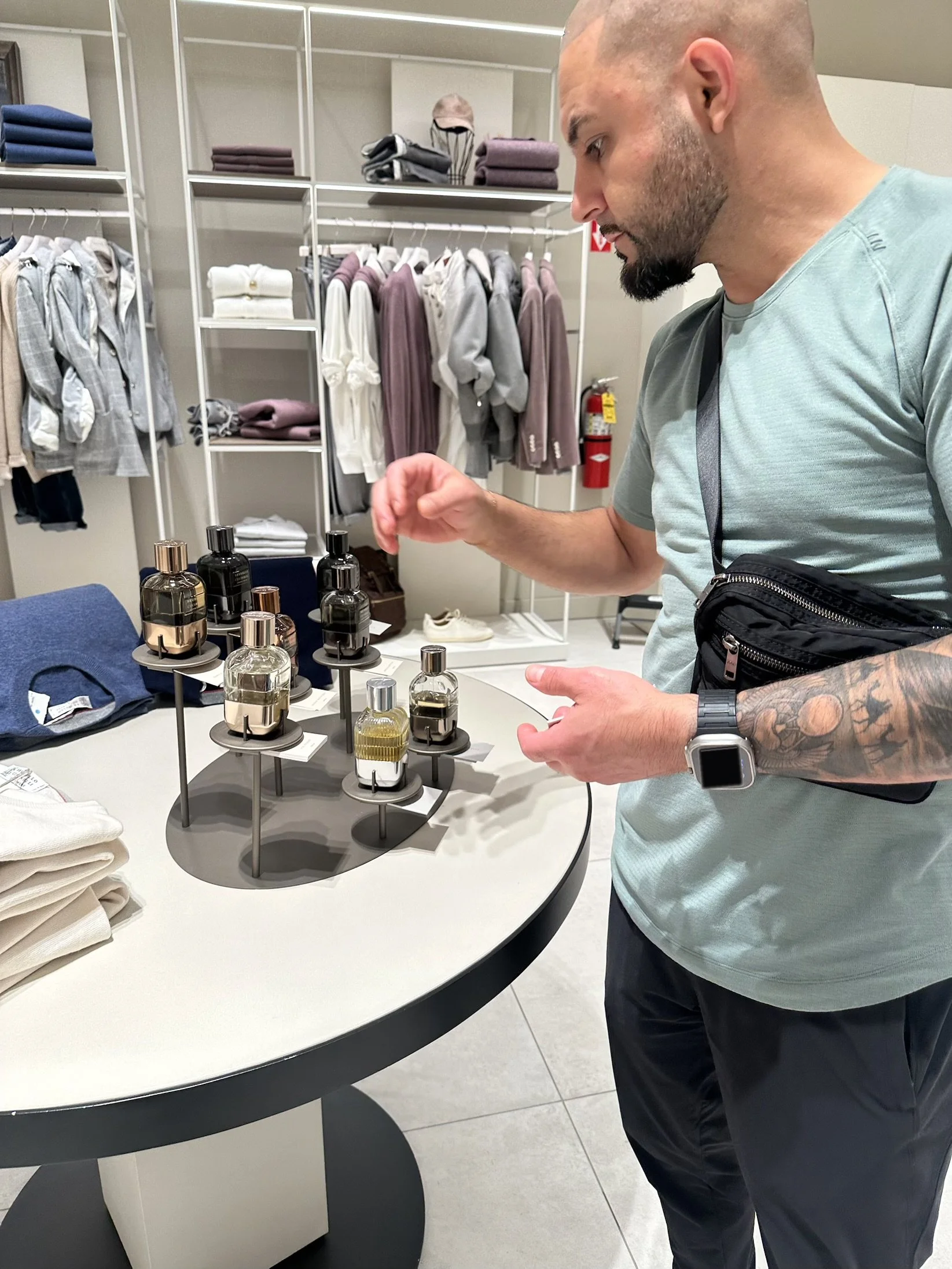 A man shopping for fragrances in a clothing store, examining perfume bottles on a round display table.