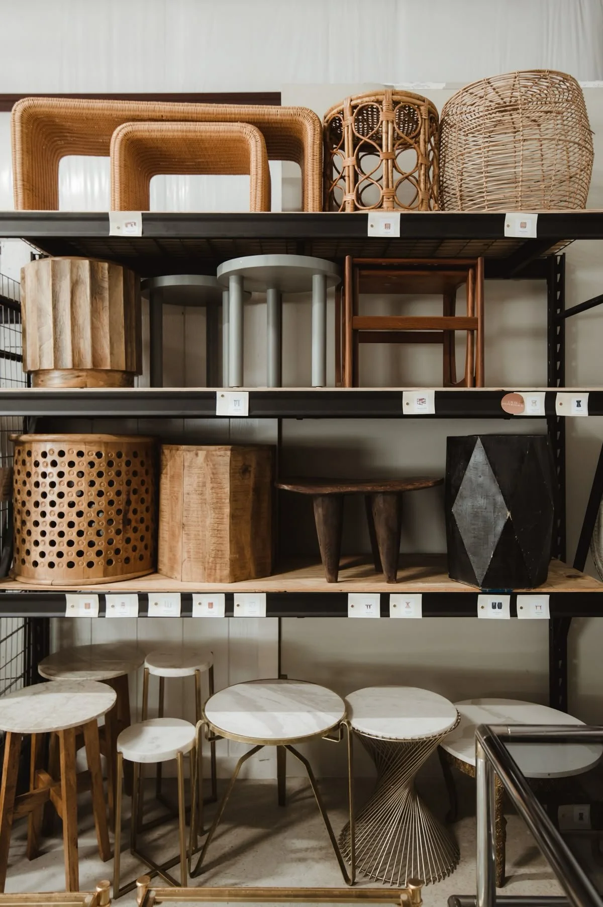 Display shelves with various wooden and rattan furniture pieces including tables, stools, and storage units.