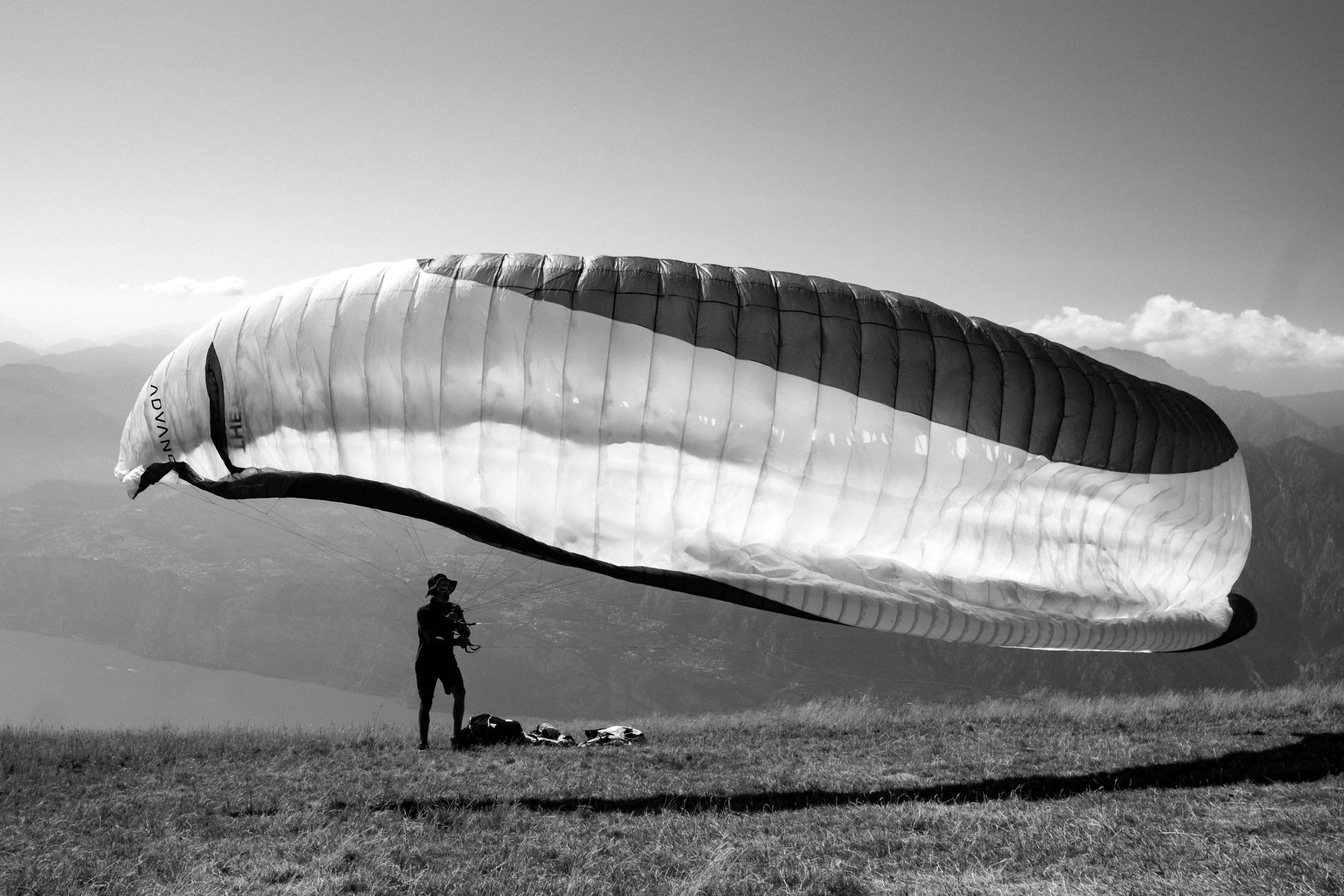 Person mit aufgespanntem Gleitschirm auf einer Wiese vor einer Berglandschaft.