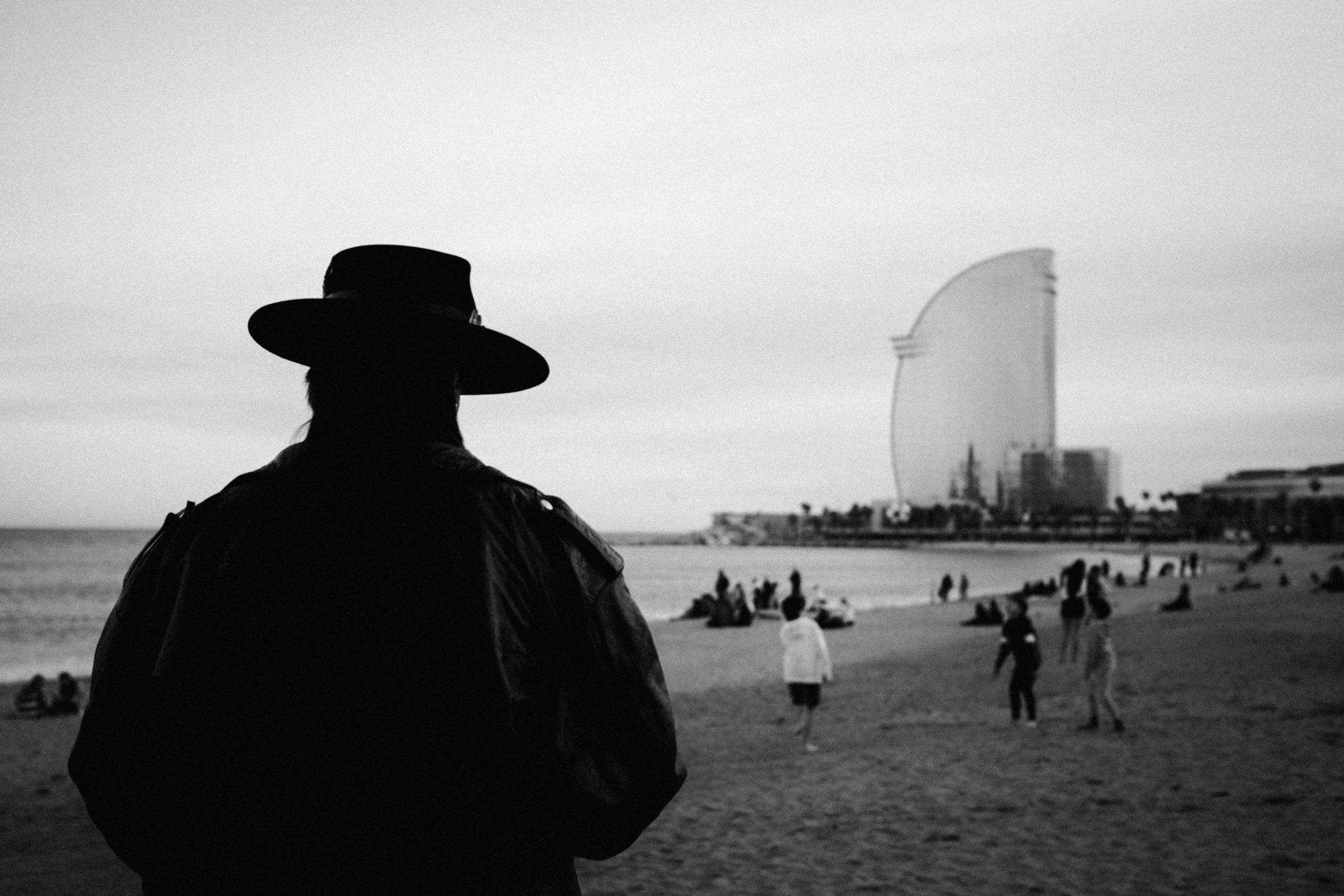 Person mit breitkrempigem Hut blickt über einen belebten Strand.