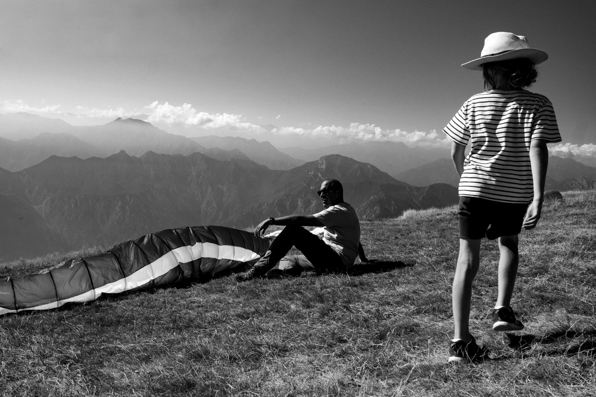 Person mit Hut blickt auf einer Bergwiese zu einem ausgelegten Gleitschirm.
