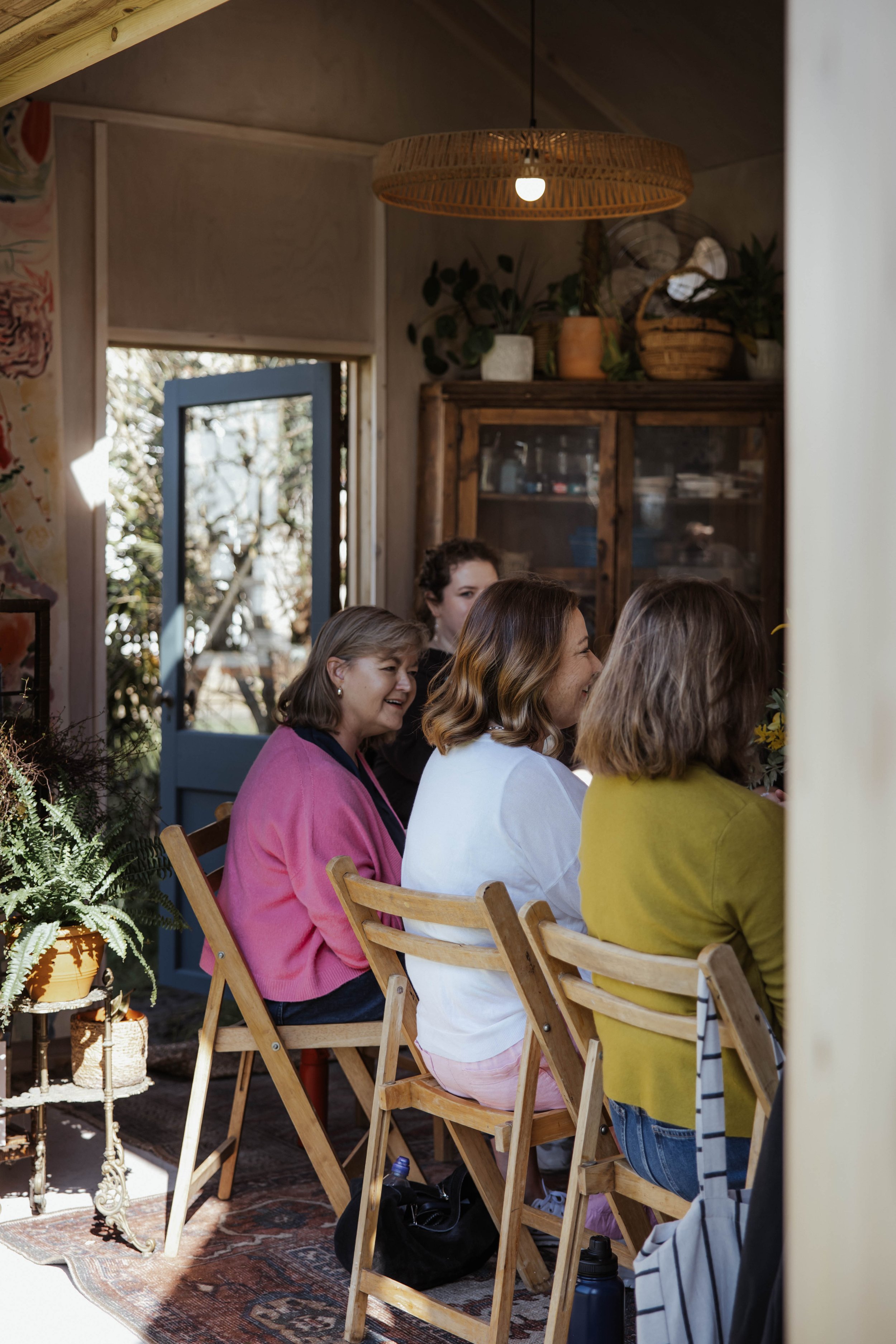 A group of women sitting at the studio table, about to do a communal painting session at a creative pause