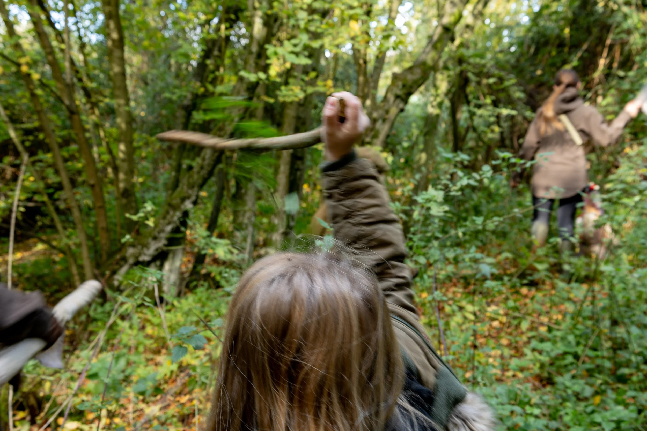 Two people in a dense, green forest, one is holding a stick. Beating in the woodlands