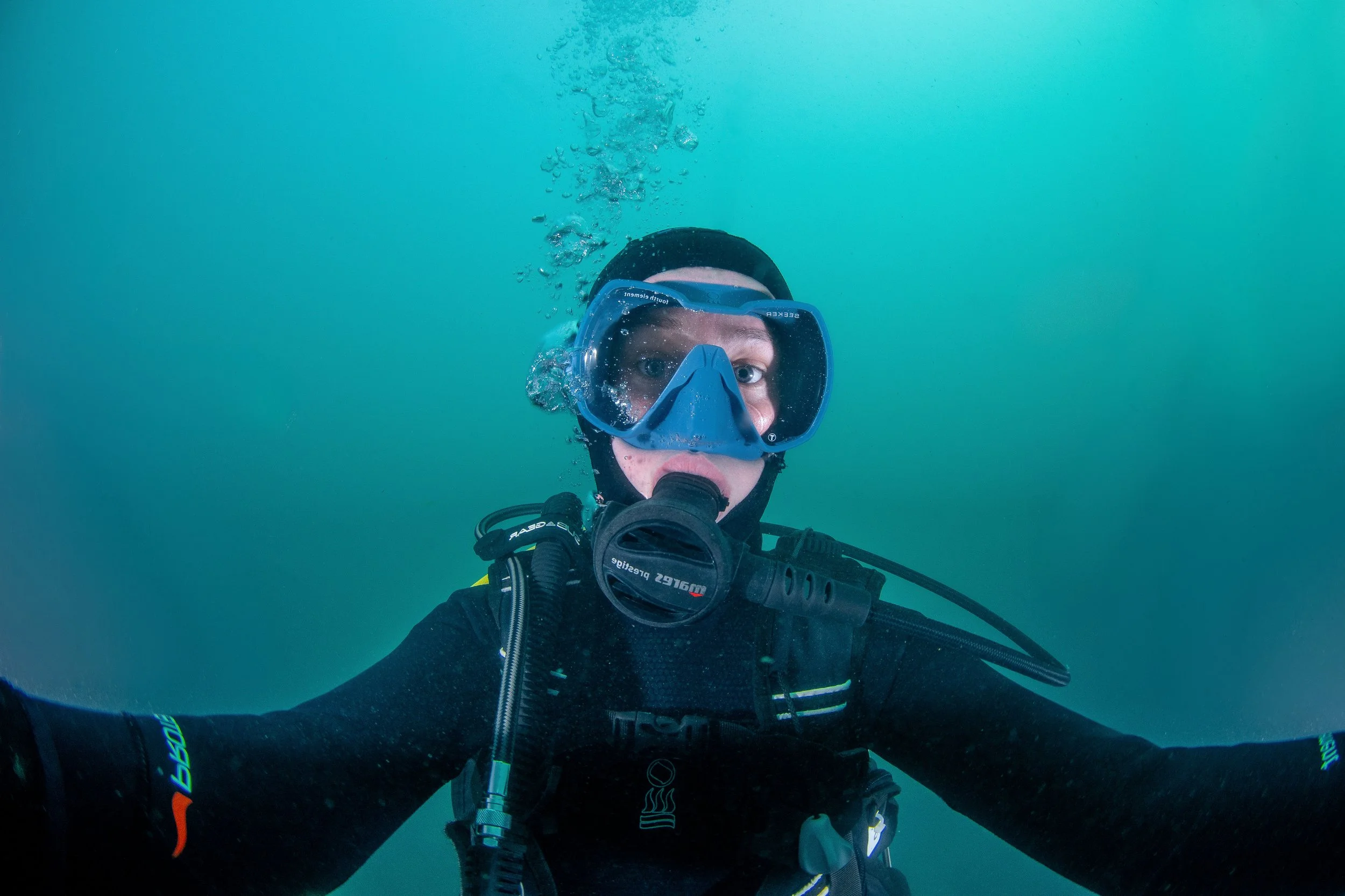 Close-up of a scuba diver wearing a mask and breathing gear underwater, with their arms extended. underwater selfie