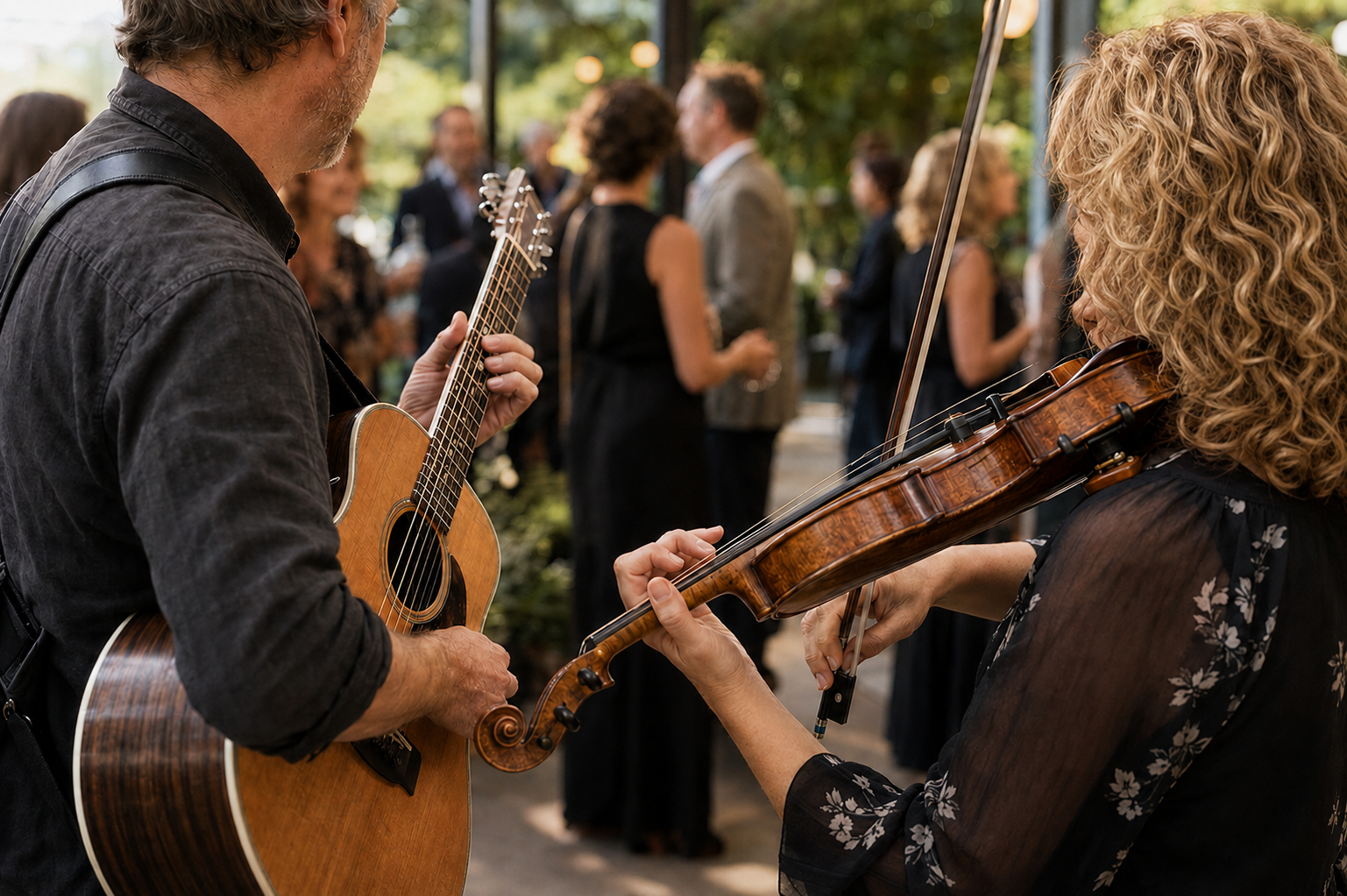 Musicians playing guitar and violin at an outdoor social event with people mingling in the background.