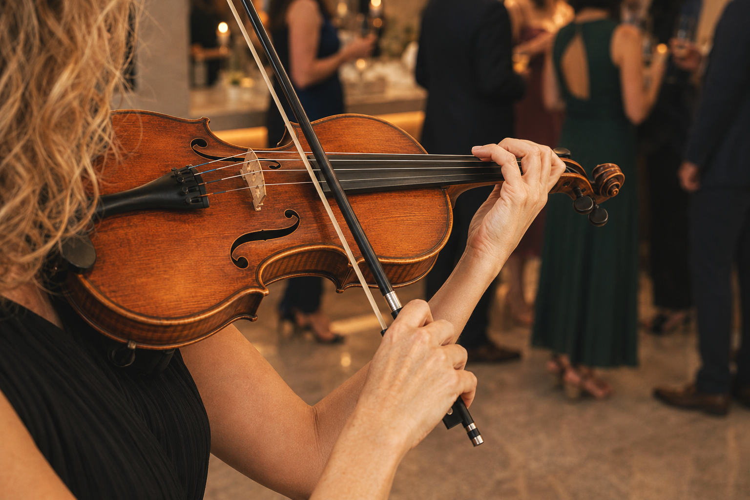 Close-up of a woman playing a violin at a formal event with people socializing in the background.