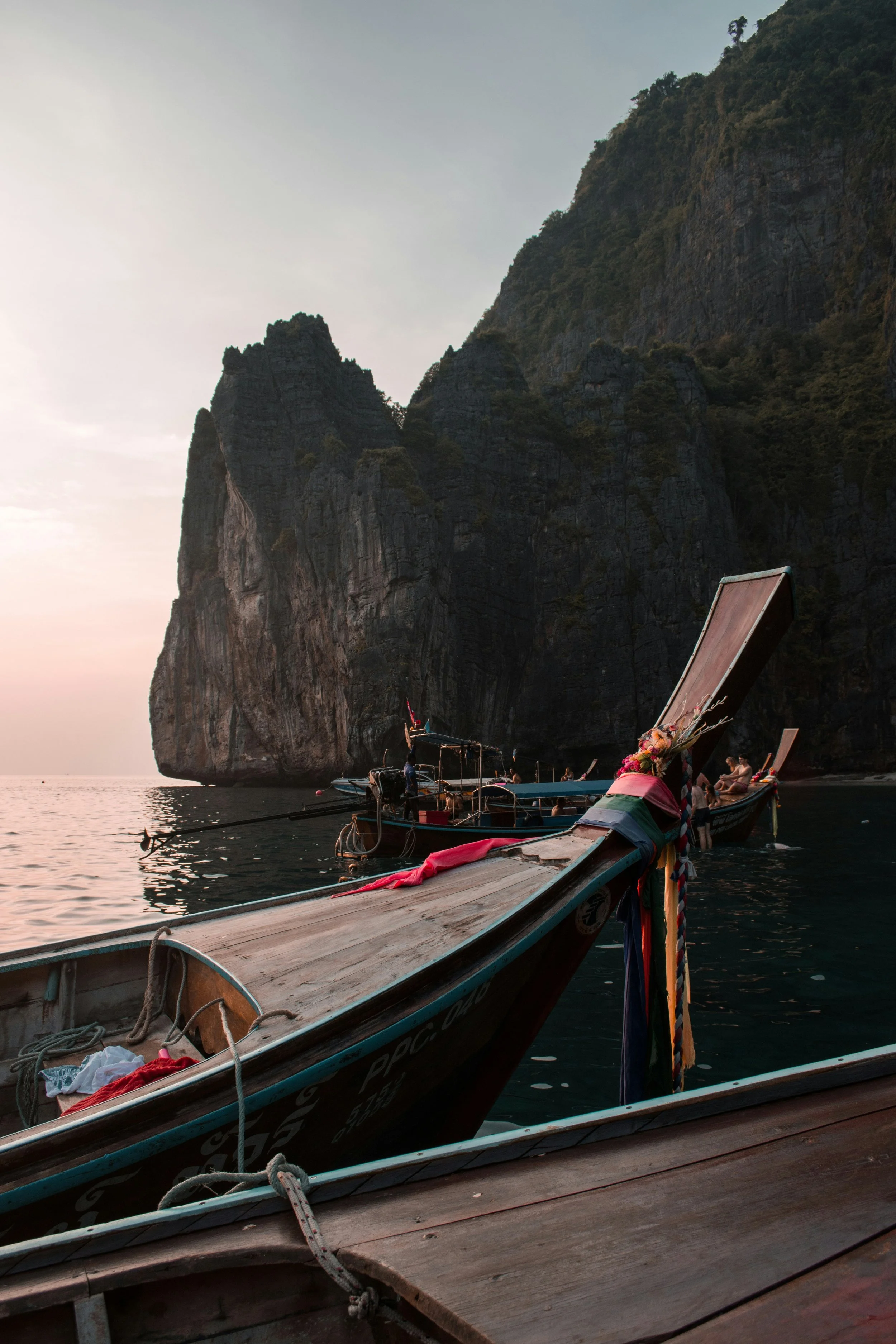 Bateaux en bois ancrés dans une eau calme devant une falaise rocheuse lors du coucher du soleil.