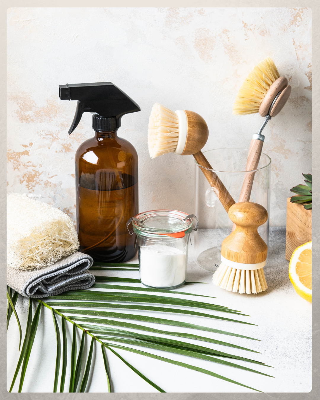 Spa or cleaning supplies including a spray bottle, brushes, cleaning cloths, a jar of white powder, and lemon slices on a white surface with green leaves.