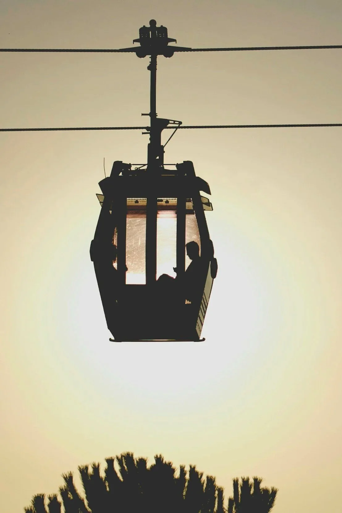 Just Travel montre la silhouette d'une cabine de téléphérique suspendue dans le ciel au coucher du soleil, avec des arbres en bas.