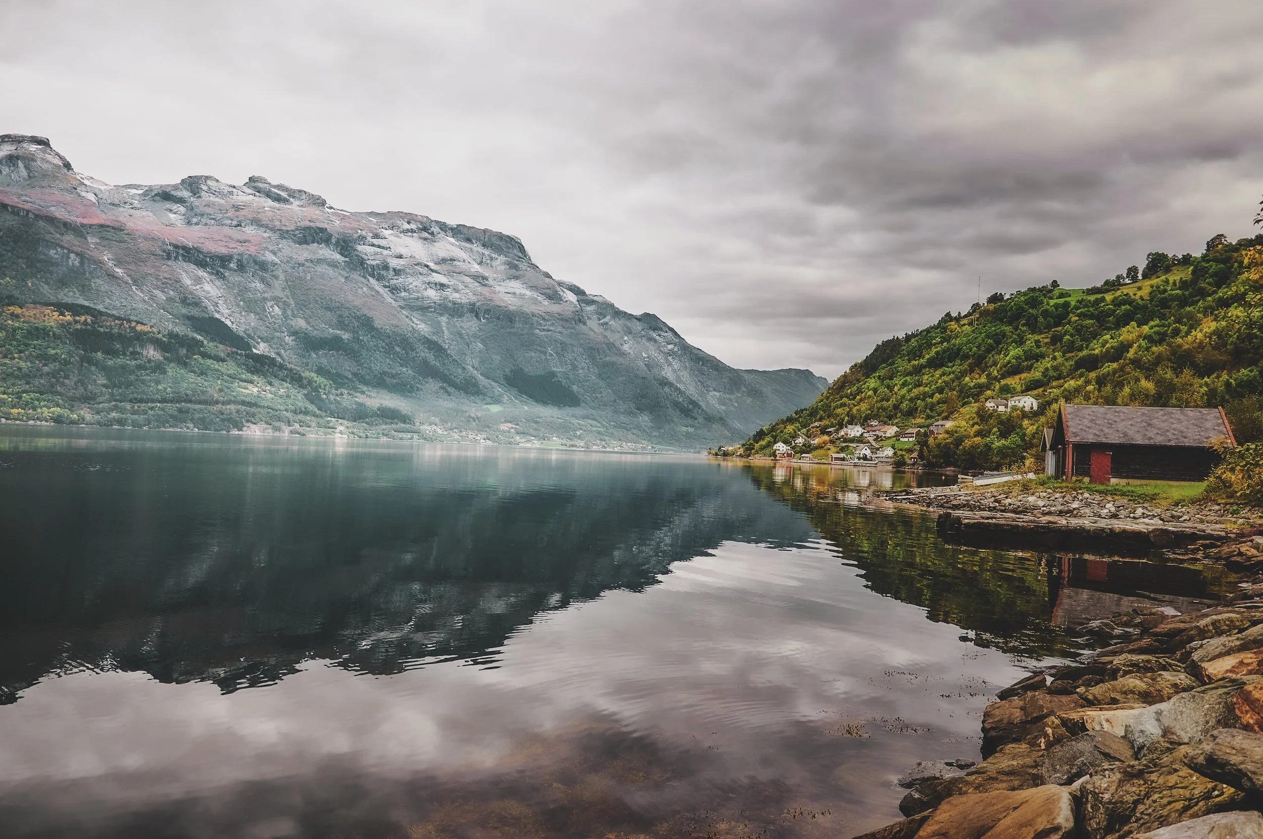 Un lac entouré de montagnes verdoyantes et de petits bâtiments, sous un ciel nuageux.