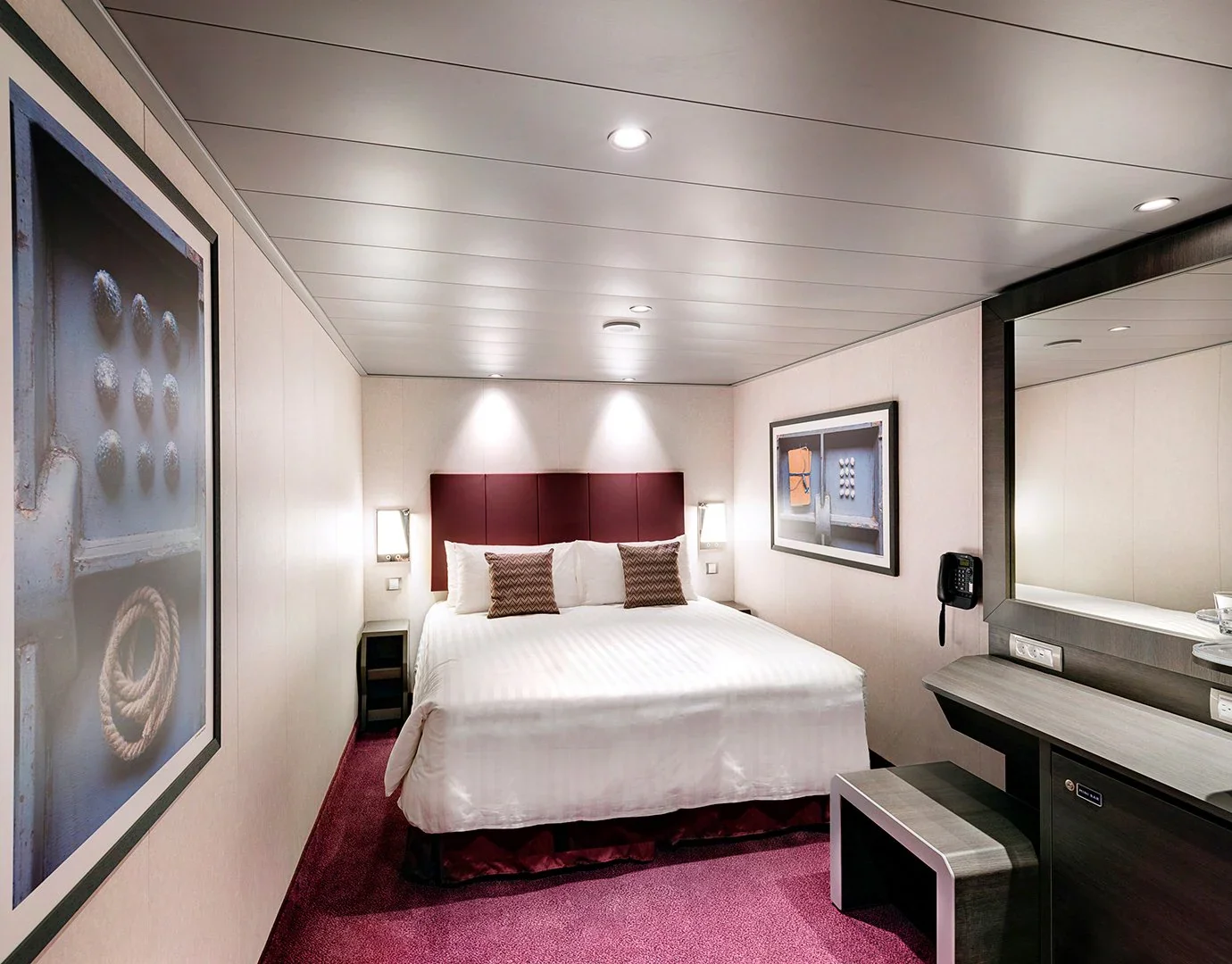 Just Travel vous propose une chambre d'hôtel avec un lit king-size, tête de lit en cuir marron, deux lampes de chevet, deux coussins décoratifs, une peinture sur le mur, un miroir et un petit bureau avec un miroir grand format et un téléphone mural.